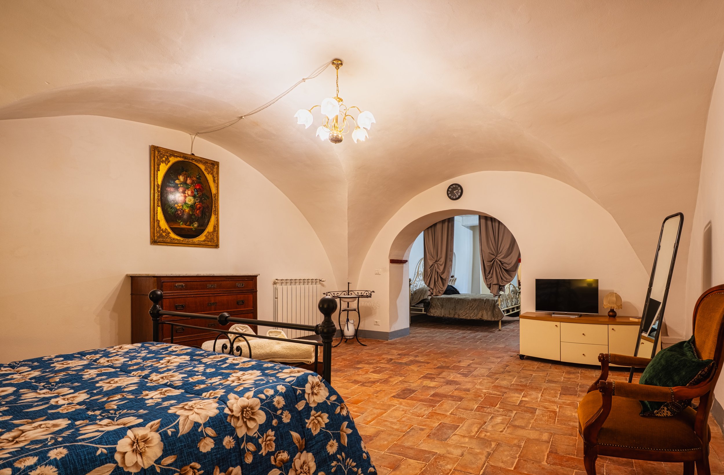 Camera arredata con letto, armadio, sedia, televisore e decorazioni in stile classico, con soffitto arcuato e pavimento in mattoni.
