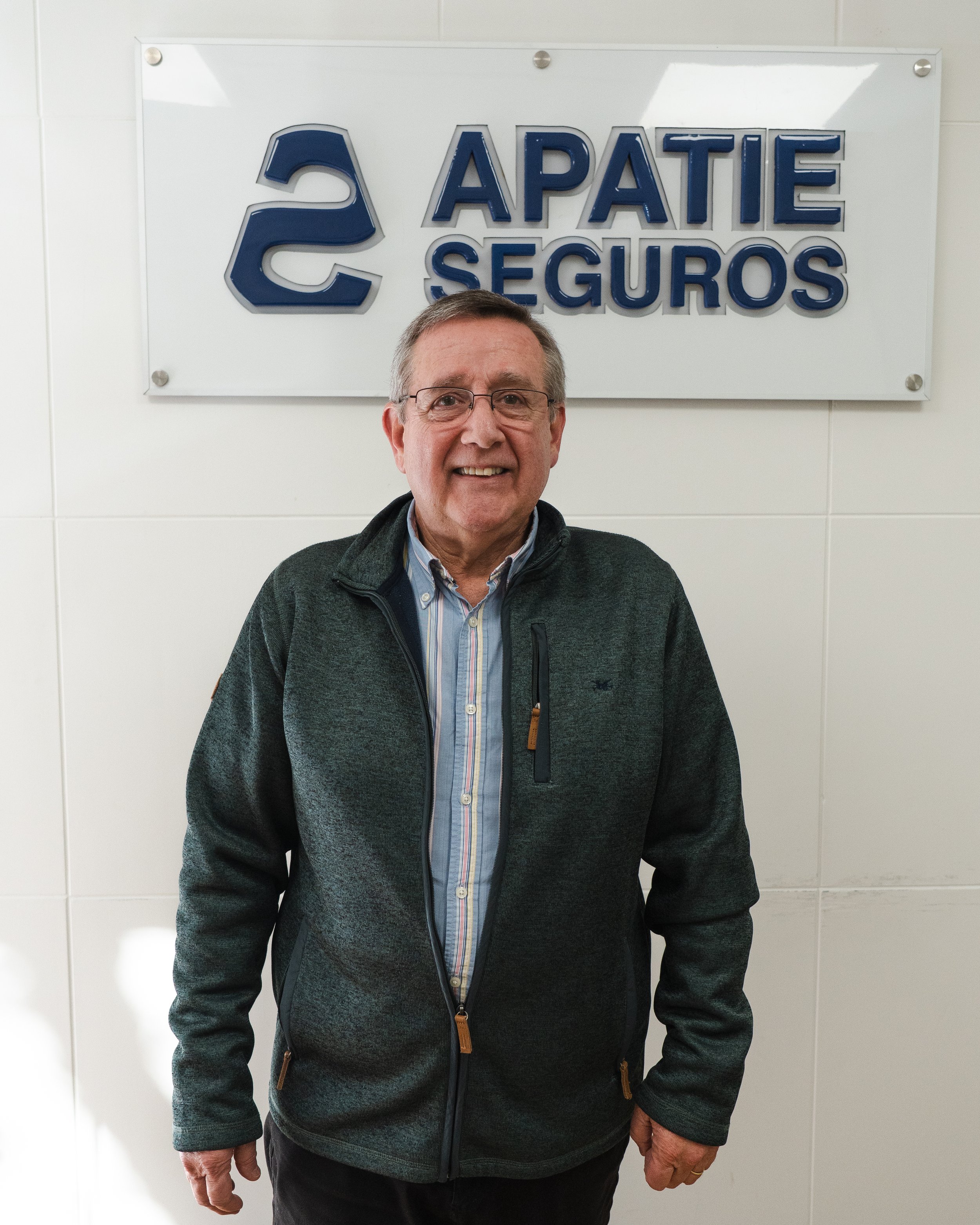 Hombre sonriendo delante de un cartel que dice 'APATIE SEGUROS' y tiene un logotipo con la letra S.