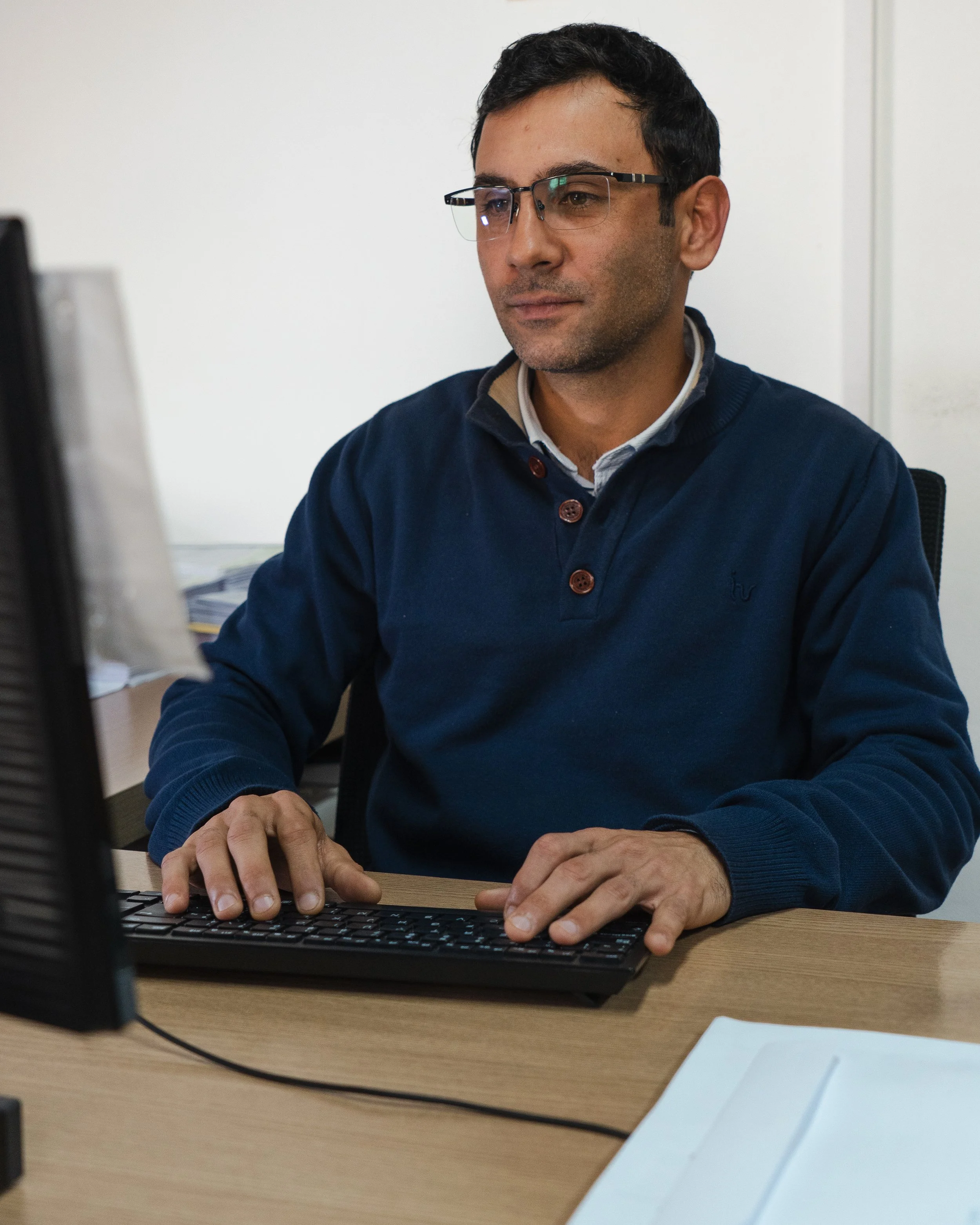 Hombre sentado en escritorio trabajando en una computadora portátil.