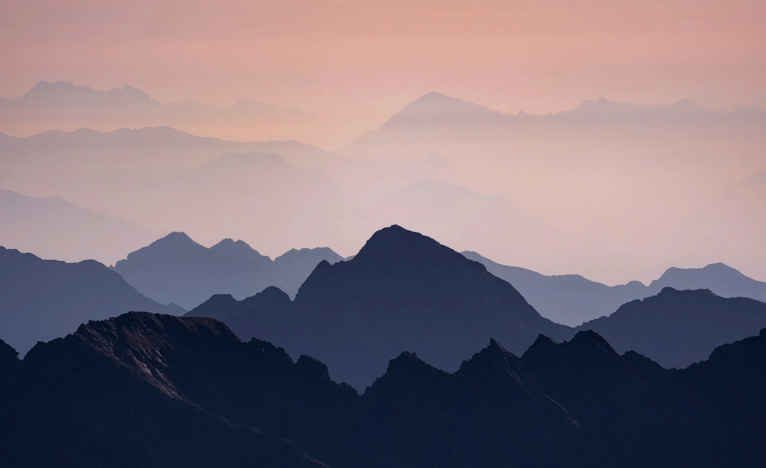 Multiple layers of mountain silhouettes fading into the distance during twilight, with a pinkish sky.