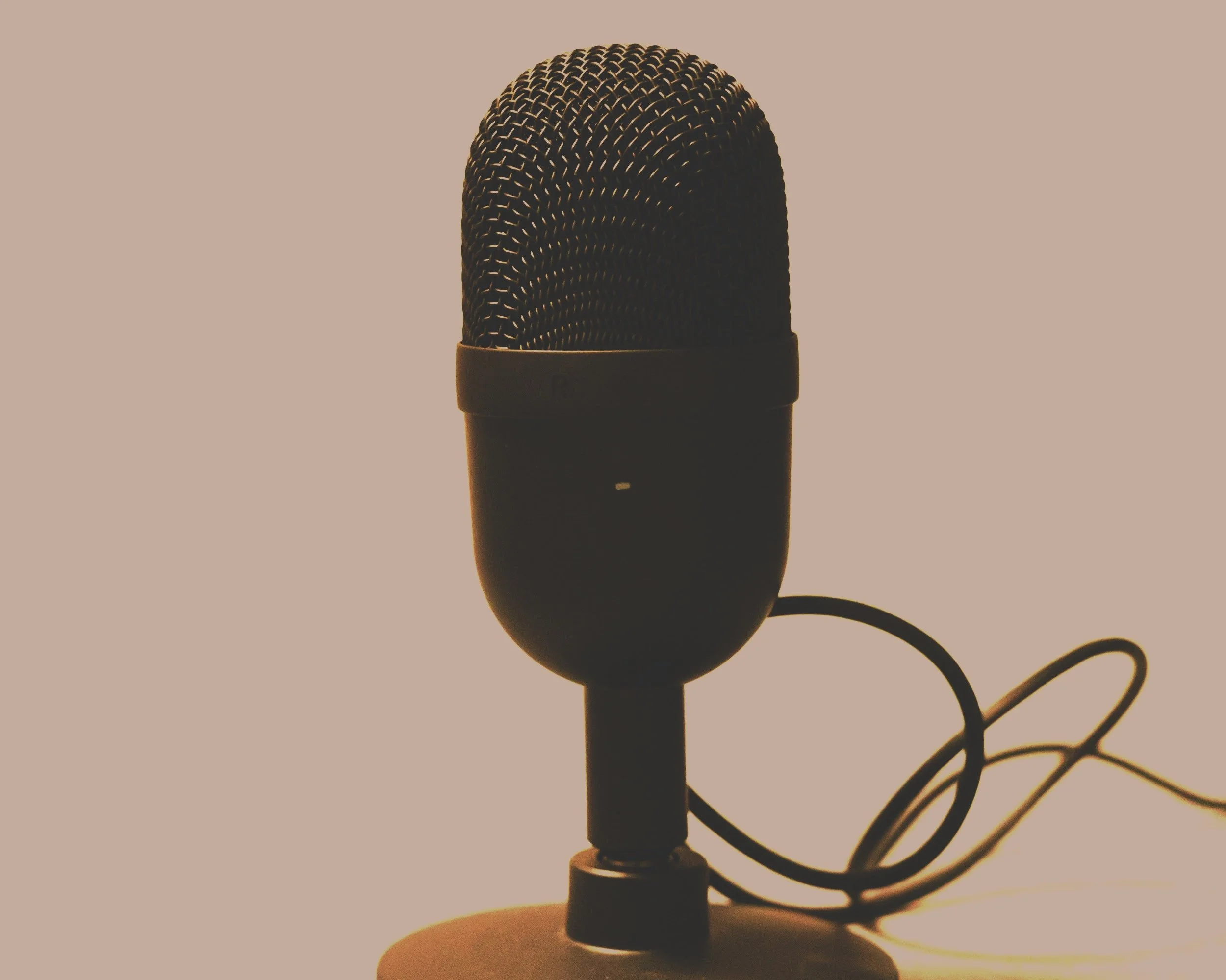 Silhouette of a wired microphone on a stand with a plain background.