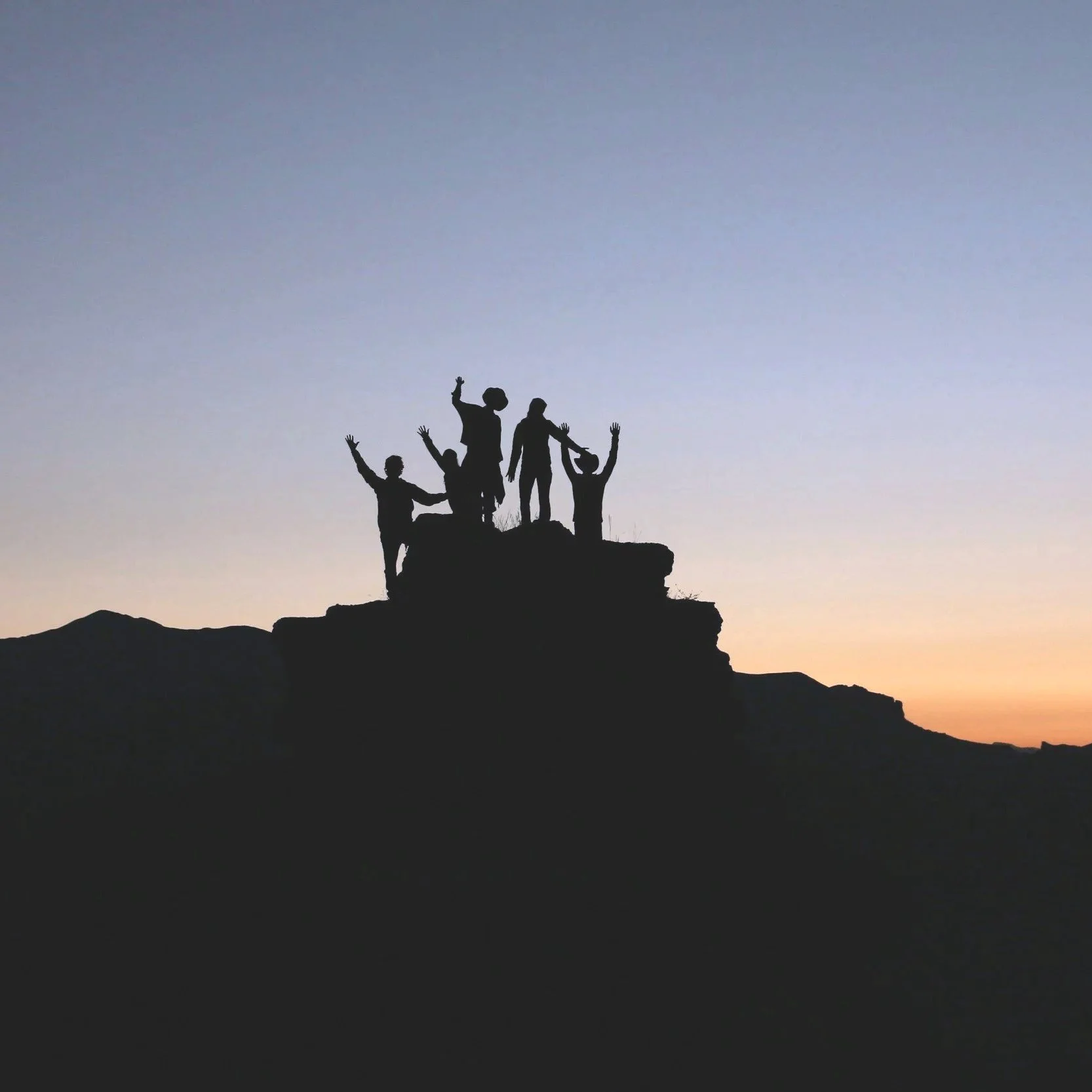 Silhouette of five people celebrating on a hilltop at sunset.