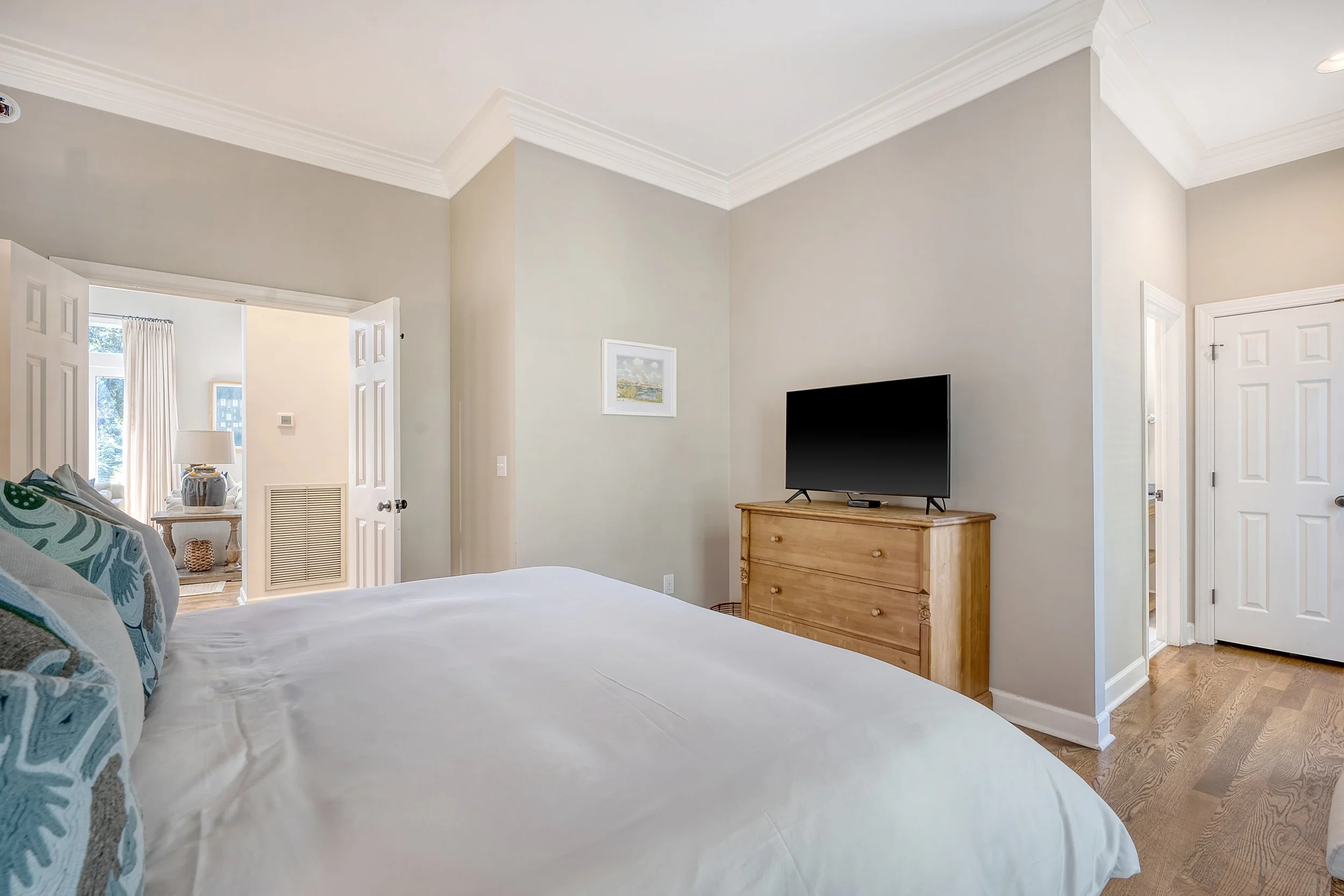 Bedroom with a bed, a wooden dresser with a TV on top, and a doorway leading to an adjoining room.