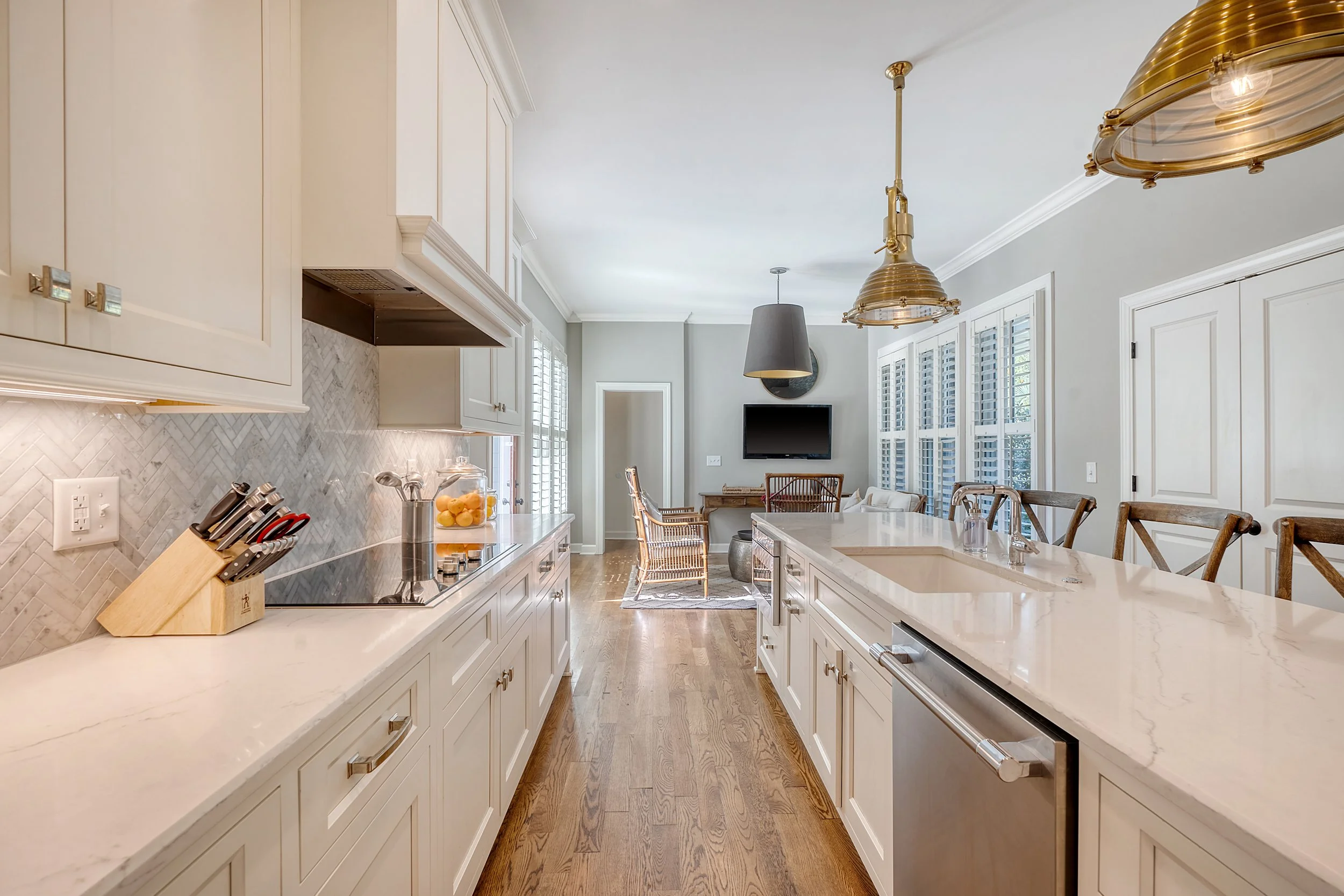 Kitchen with white cabinets, marble countertops, wooden flooring, and a view into a living space with chairs, a small table, and a wall-mounted TV.