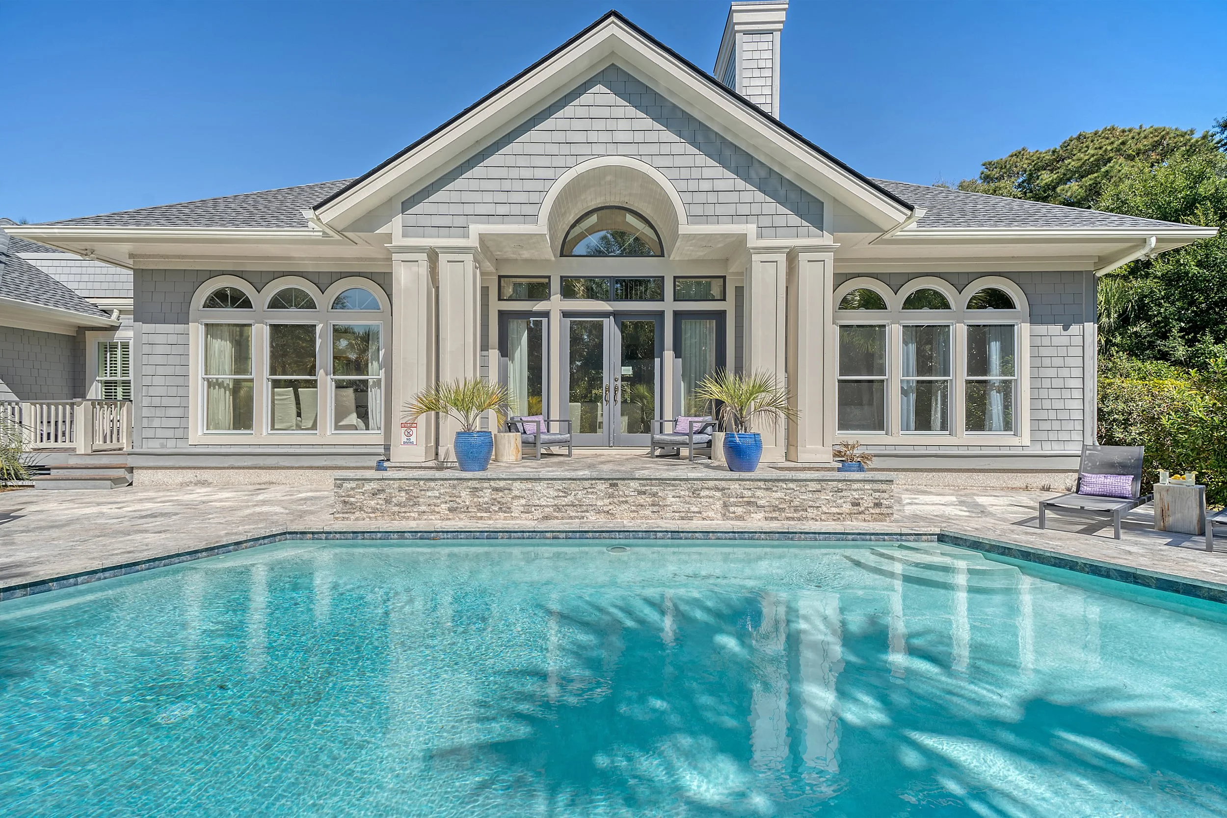 A luxurious house with a swimming pool in the backyard, featuring a set of glass doors, decorative windows, and outdoor seating with potted plants.