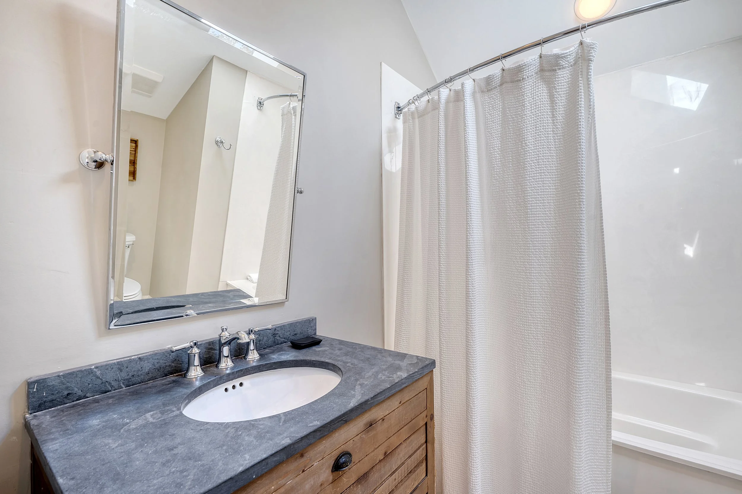 Bathroom with a mirror, vanity with a sink, faucets, soap dish, shower curtain, and bathtub.