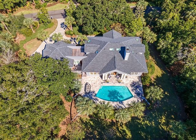 Aerial view of a large house with a swimming pool and surrounding trees in a lush yard