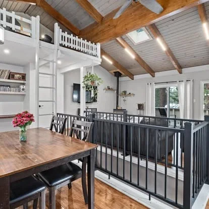 loft with ladder in main living area above table and railing around stairs