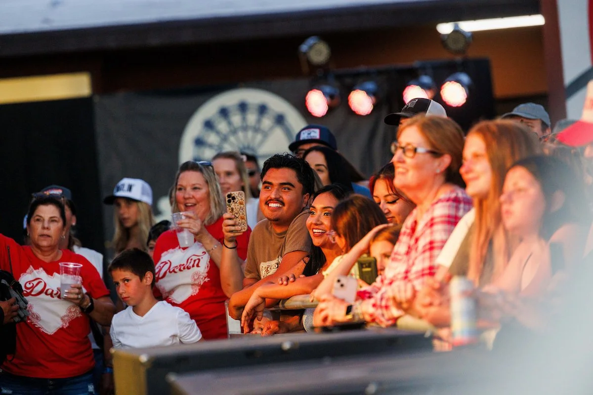 Crowd of people at a live outdoor event, smiling and enjoying the show.