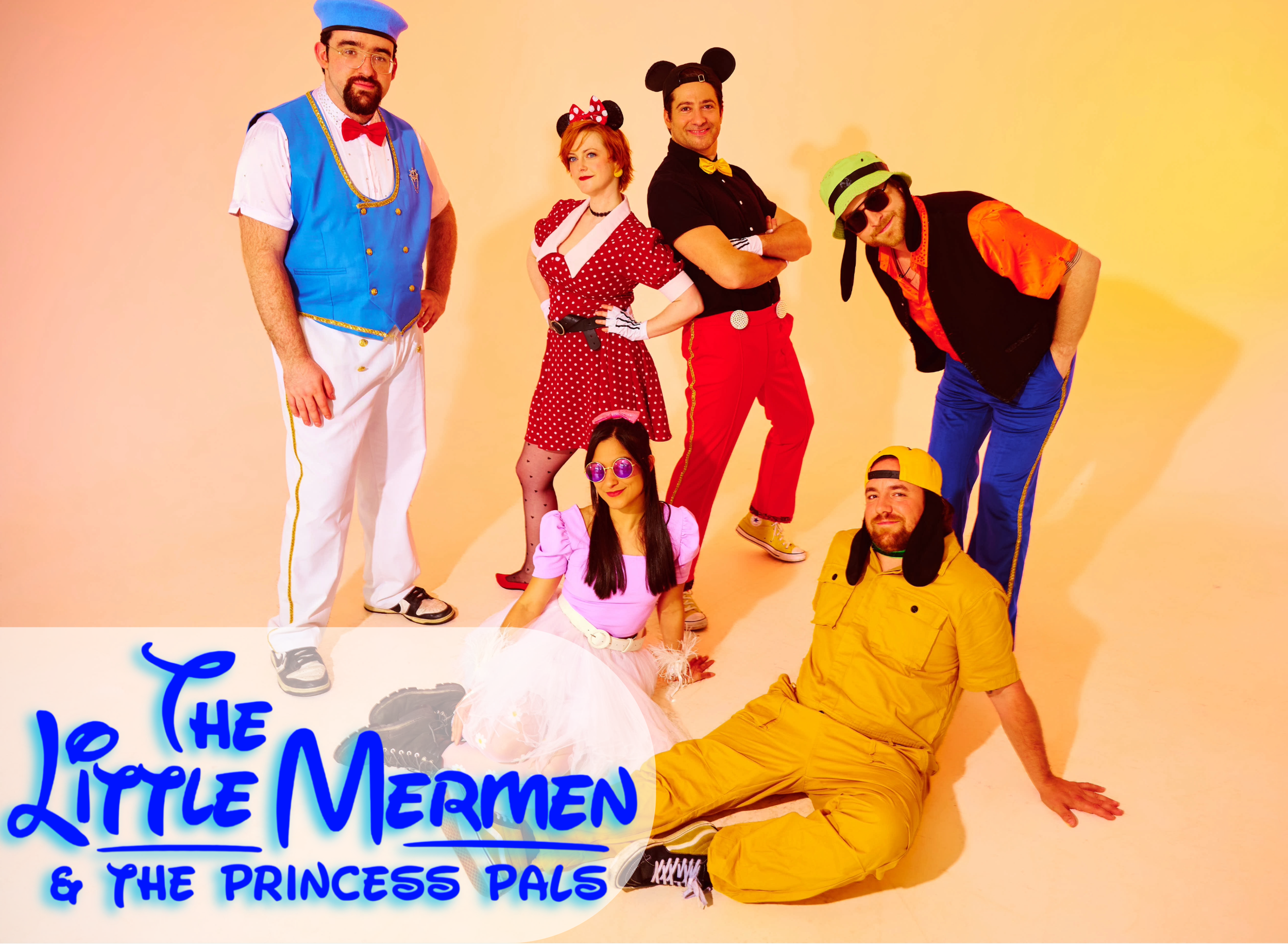 Group of five people dressed in colorful, playful costumes posing against a beige background. They include a man in a blue vest and white pants, a woman dressed as Minnie Mouse, a man with mouse ears, a woman in a pink dress and tutu, and a man in yellow outfit with a green hat and sunglasses.