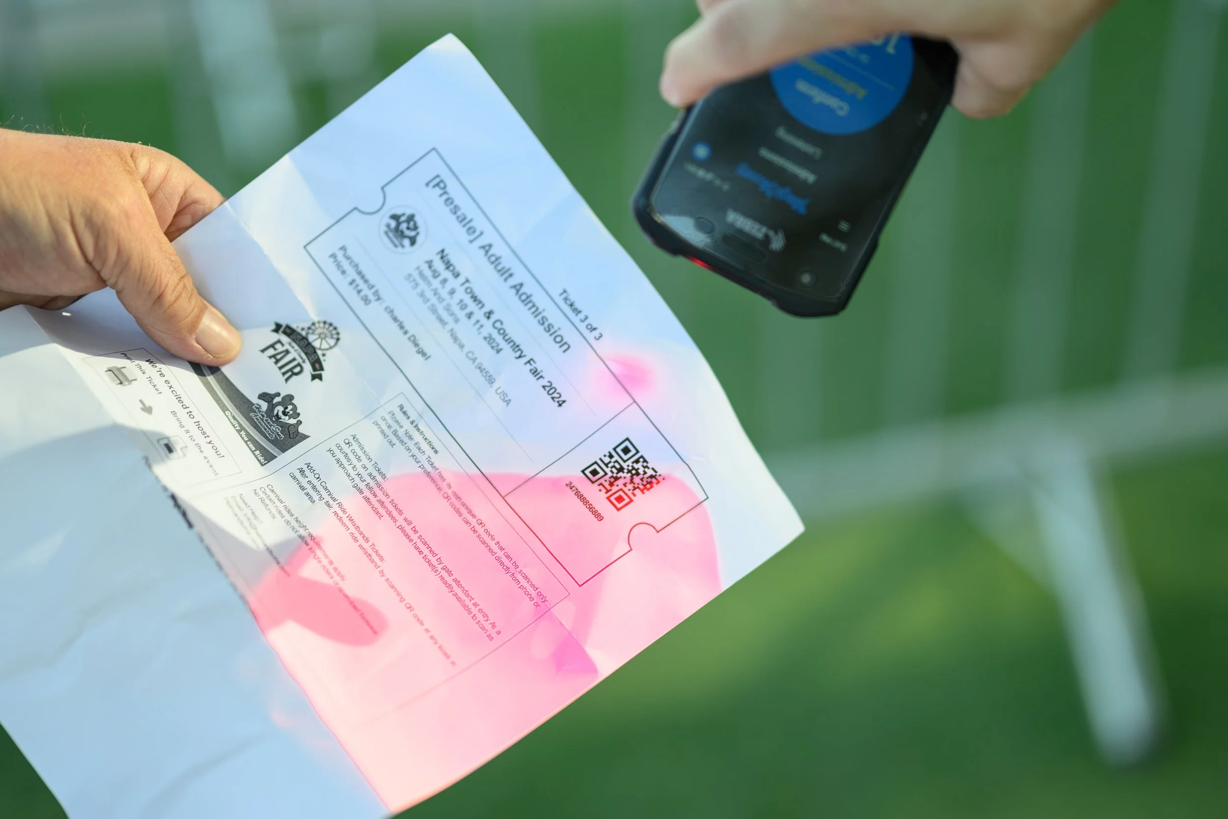 A person holding a ticket for the Napa County Fair 2024 while scanning it with a smartphone, with a green outdoor background.
