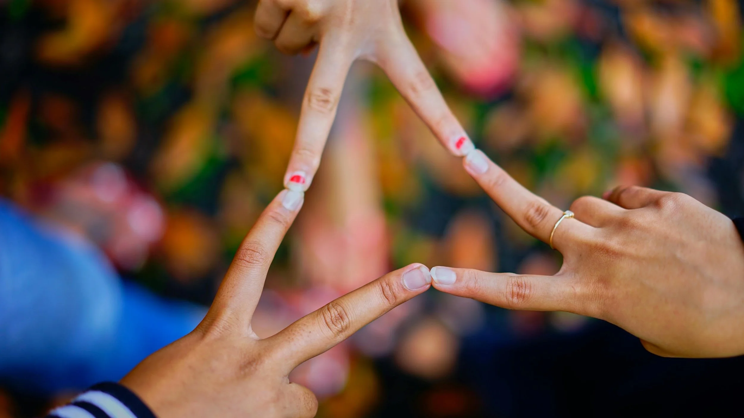 Two people making a star shape with their hands, with colorful fall leaves in the background.