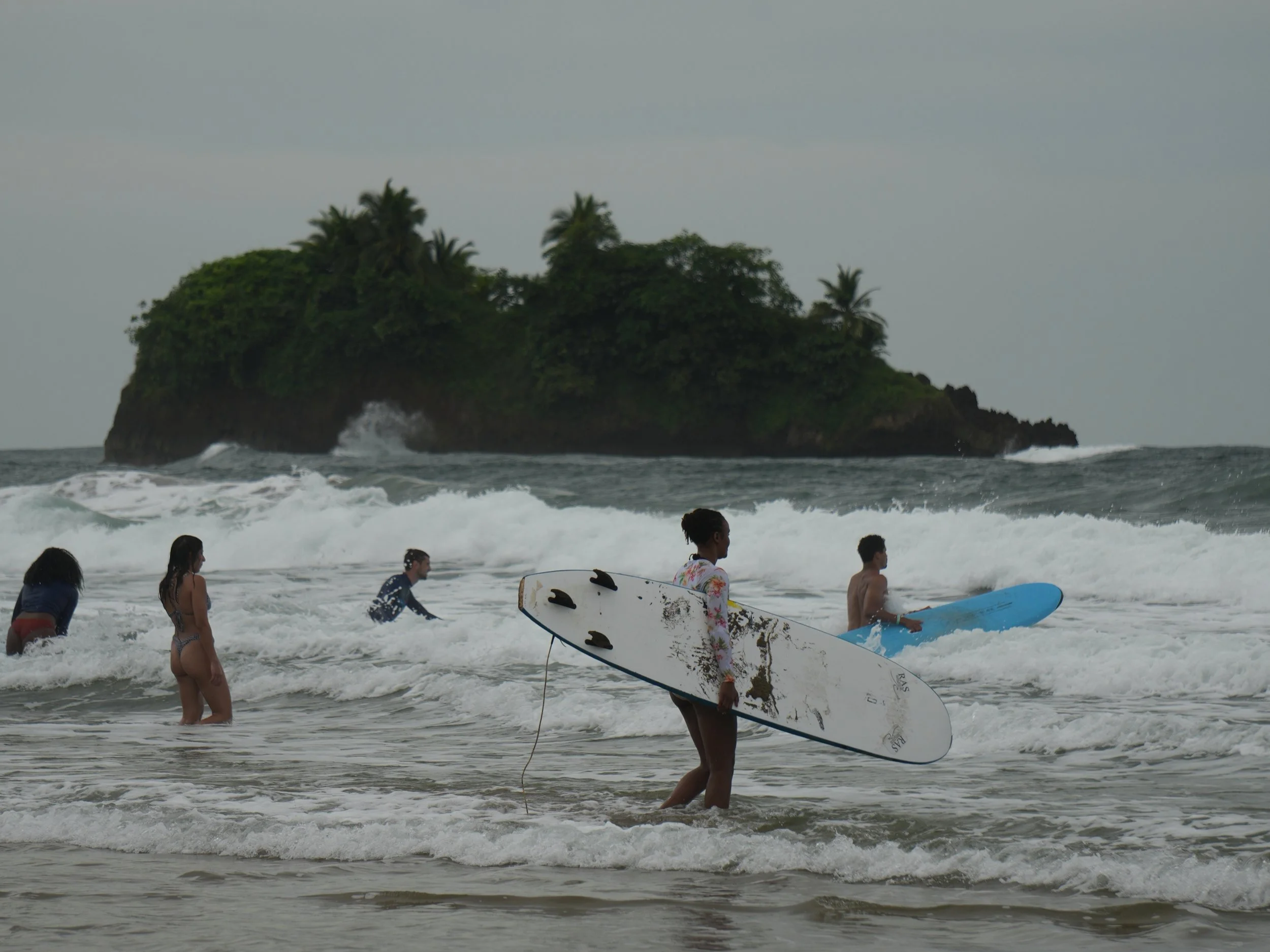 Surfers carrying boards into the ocean near a small tropical island off the Caribbean coast of Costa Rica.