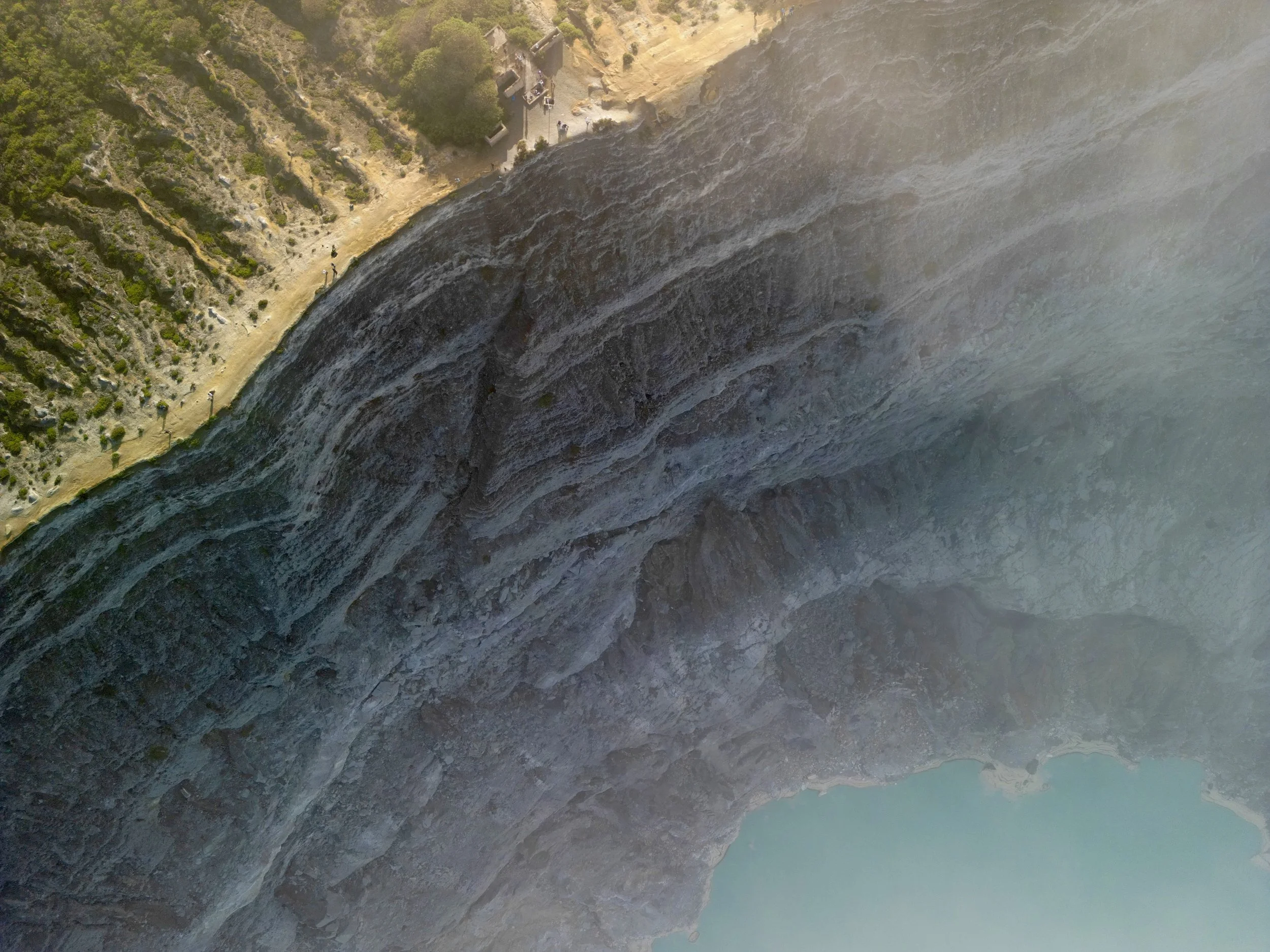 Aerial view of a turquoise crater lake surrounded by Ijen volcanic rock formations in Indonesia, photographed by drone.