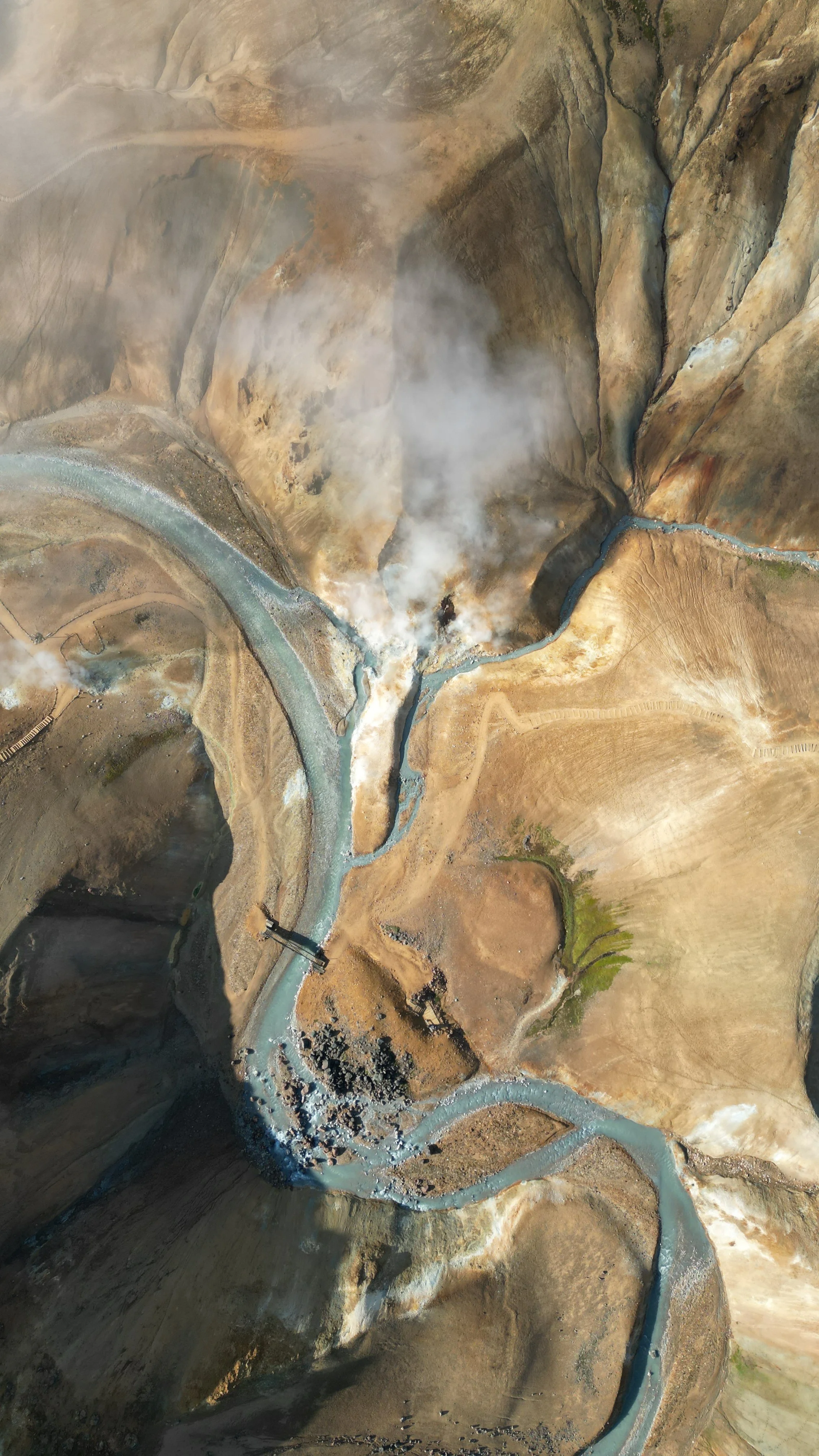 Aerial view of geothermal landscape with steaming vents and eroded earth, highlighting natural patterns and color variation in Iceland.