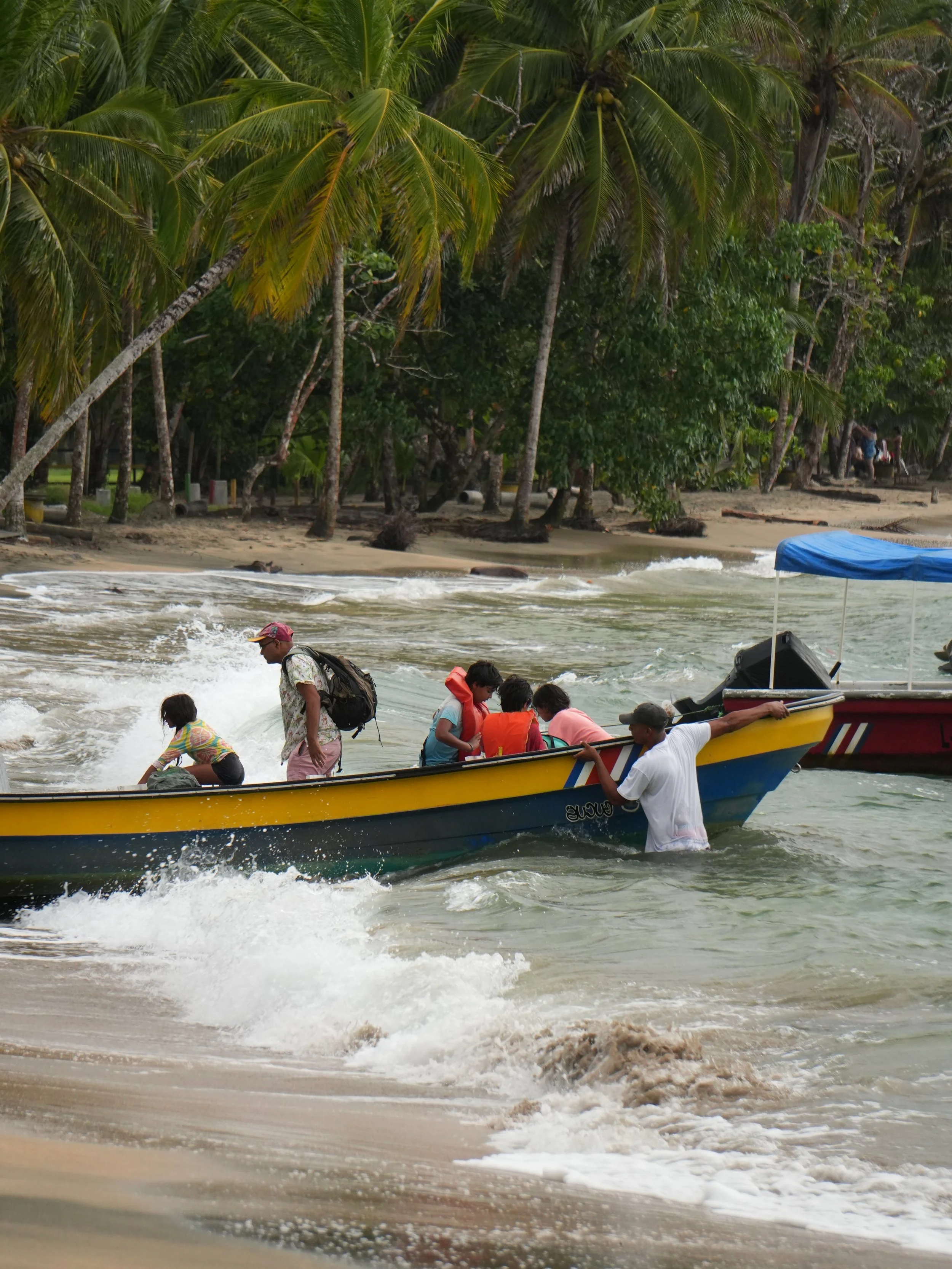 People arriving by small boat on a tropical beach lined with palm trees on the Caribbean coast of Costa Rica, capturing daily life and coastal travel moments.