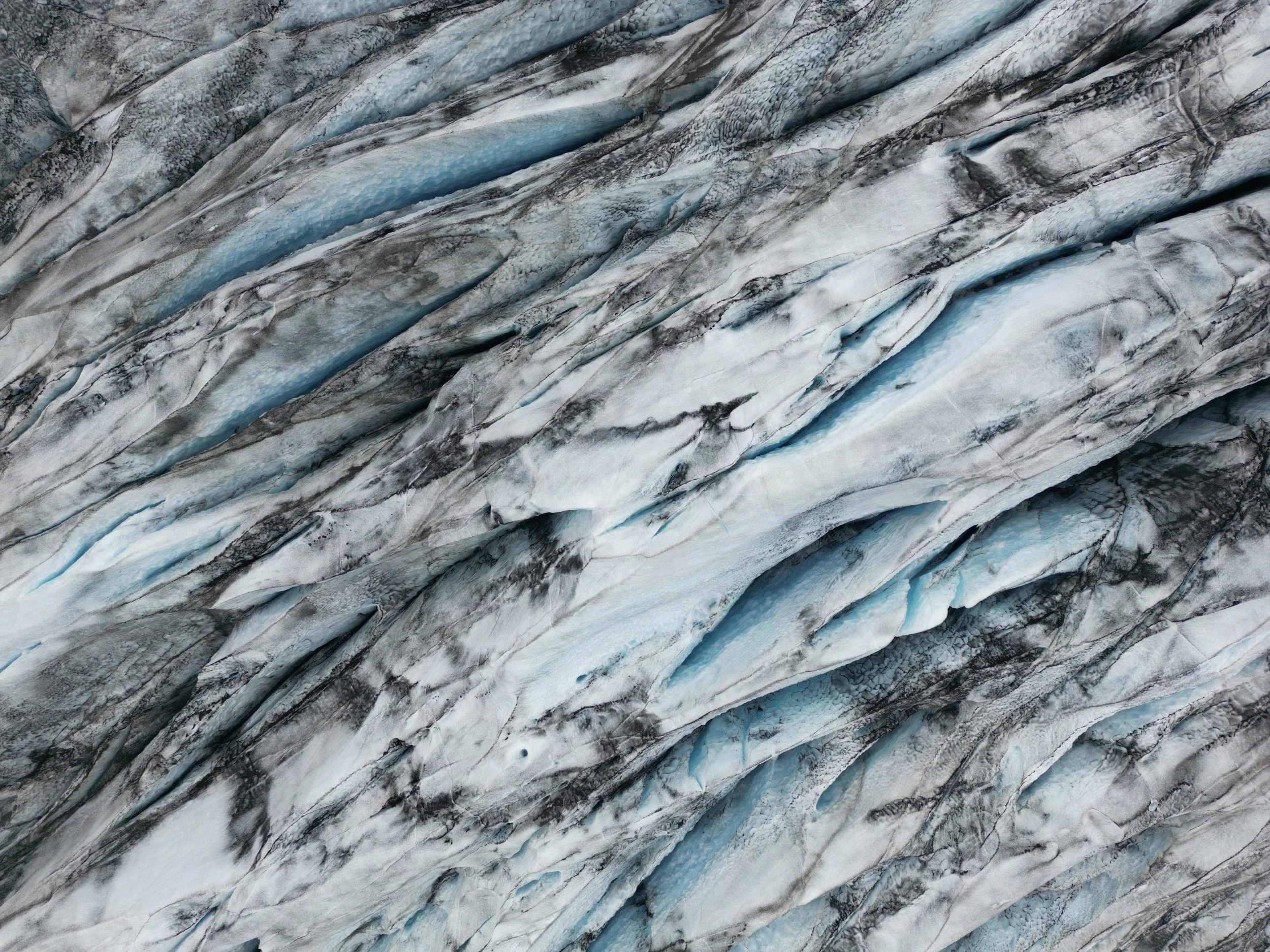 Close-up aerial view of a glacier showing crevasses and ice formations in shades of white, blue, and gray.