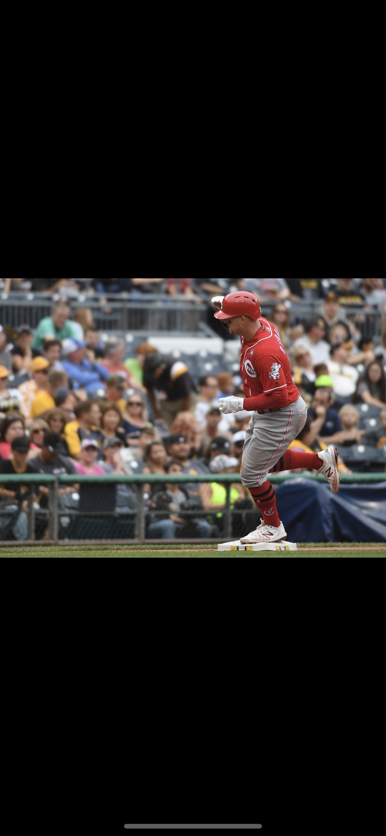 A baseball player in a red uniform running on a base during a game, with a crowd of spectators watching in the background.
