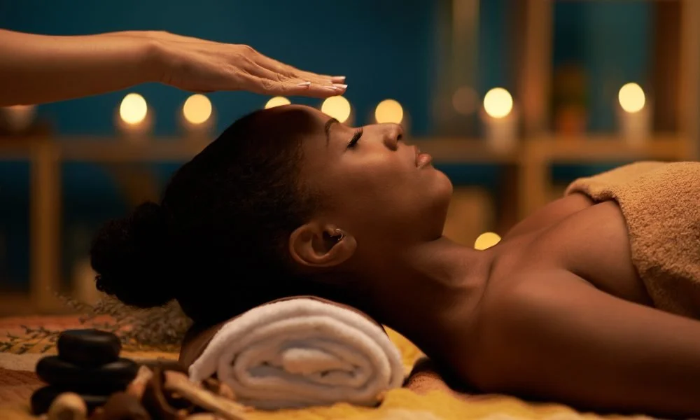 Woman receiving a back massage in a spa, lying face-up with eyes closed, surrounded by candles and spa stones.