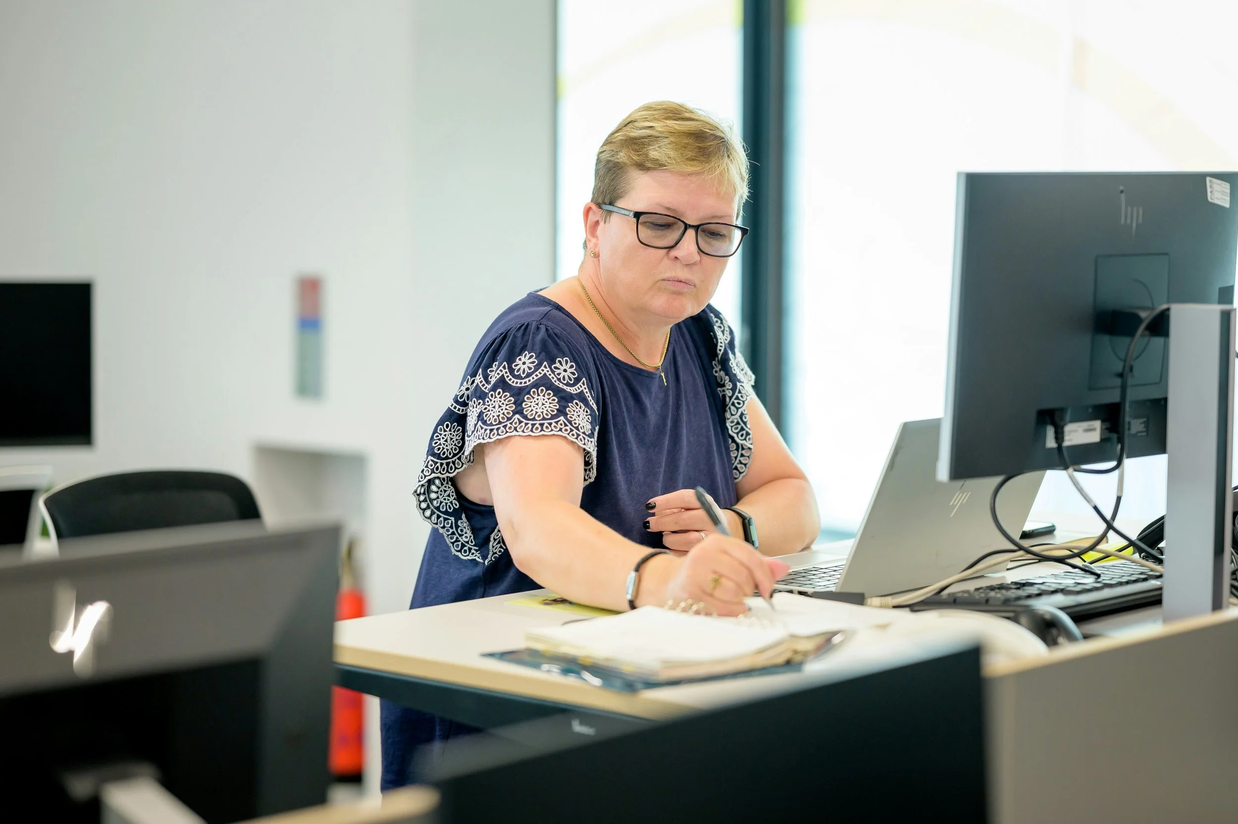 Person working at a desk, writing notes while using a laptop