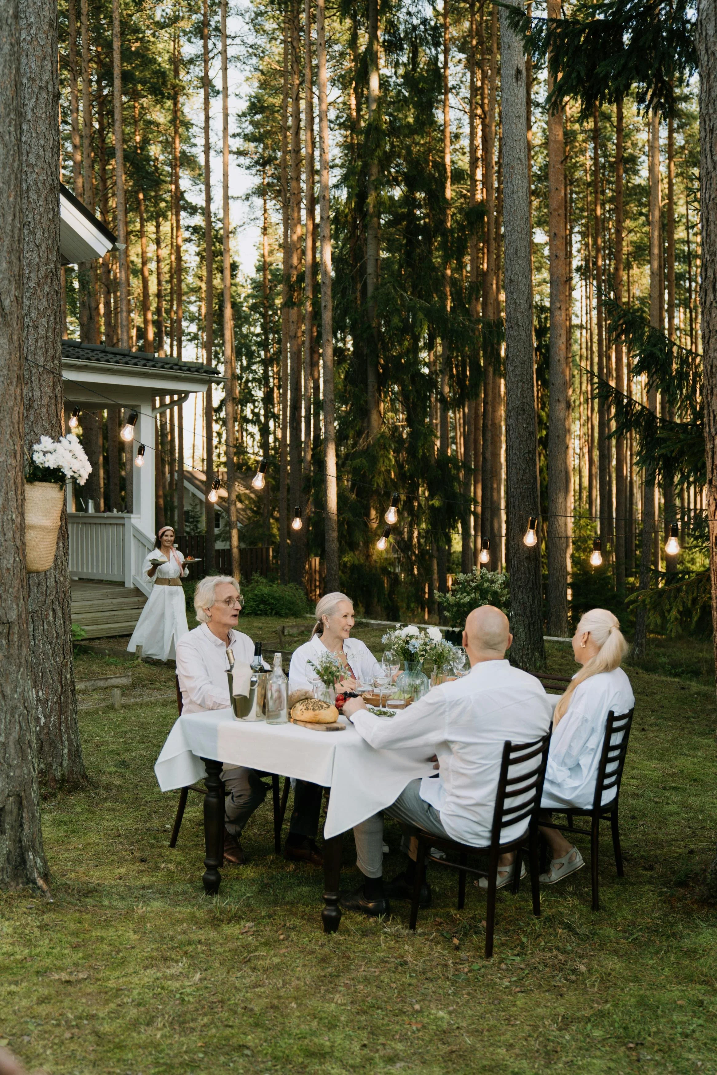 Group of adults dining together outdoors at a table set in a forest