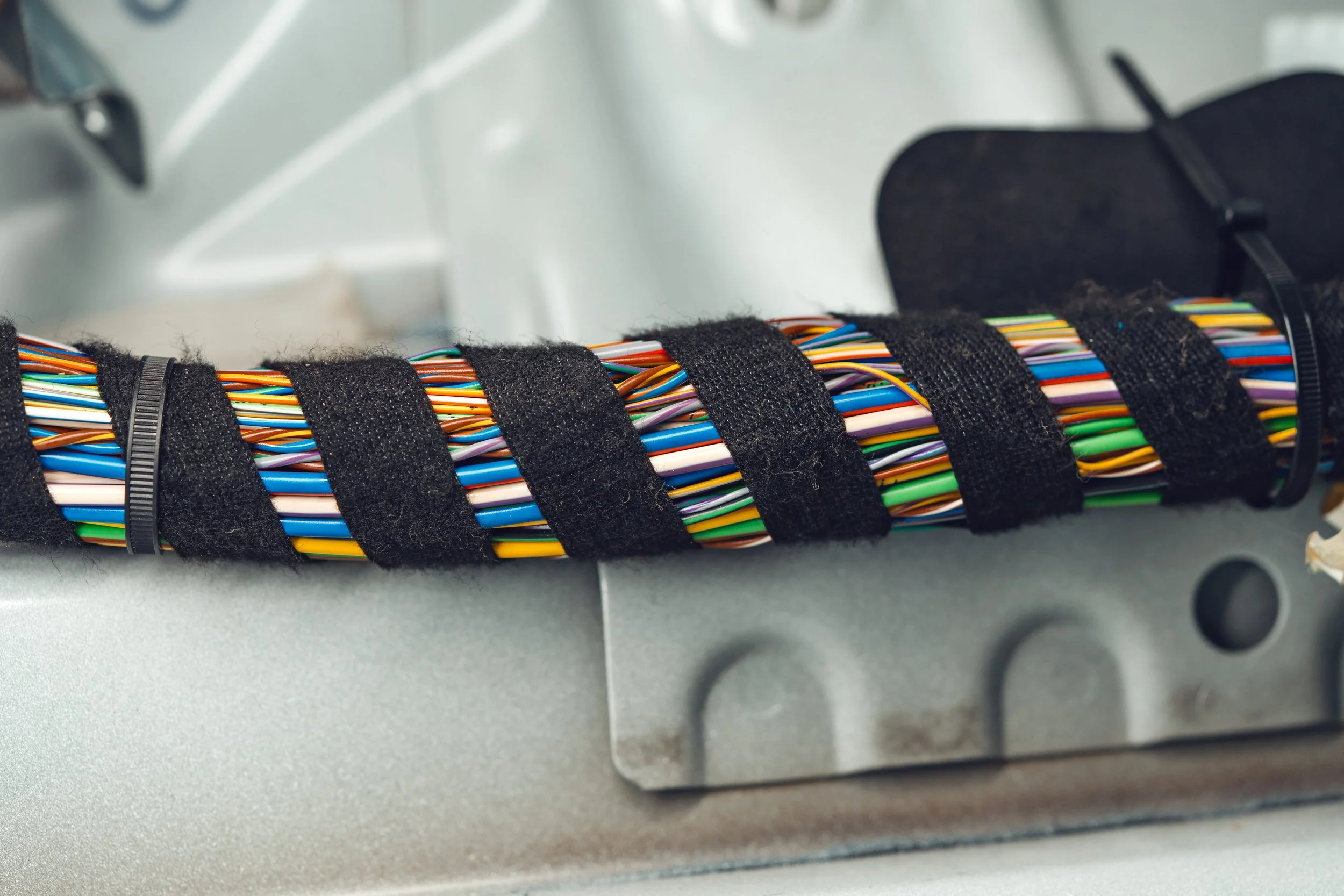 Close-up of a bundle of multicolored wires wrapped with black fabric tape inside a metal enclosure.