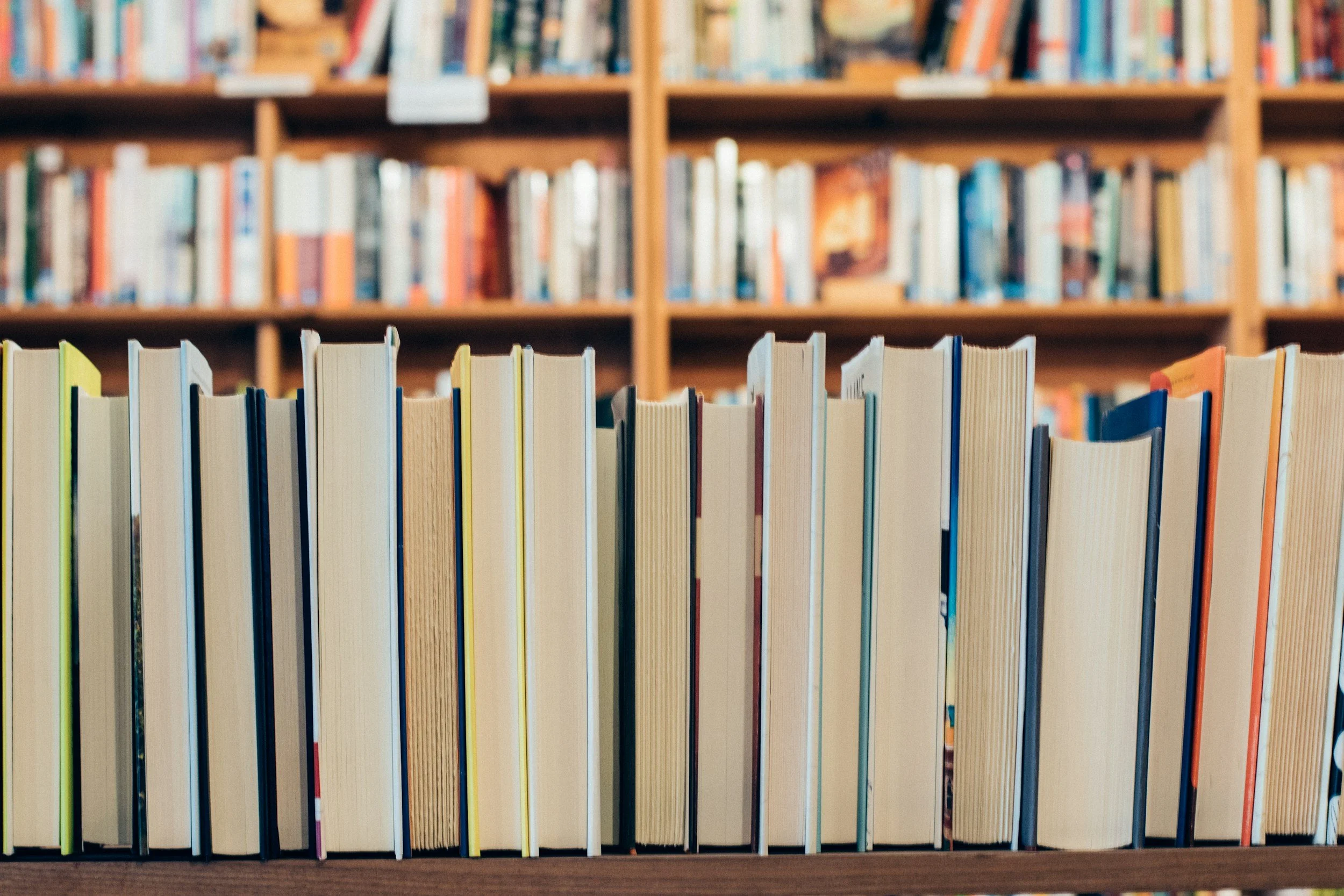 A row of books on a shelf in a library with more bookshelves in the background.