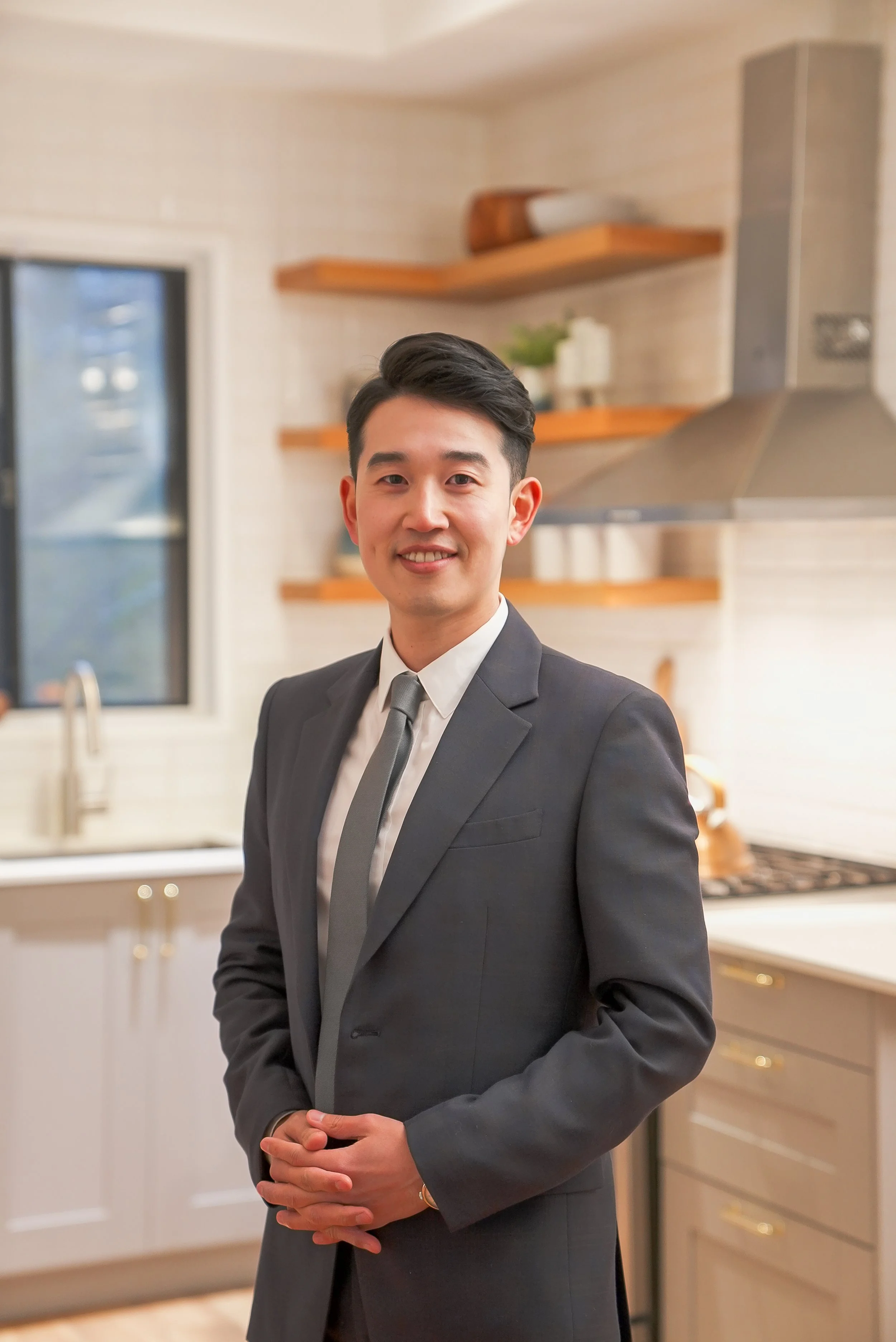 A young man in a gray suit and tie standing in a modern kitchen.