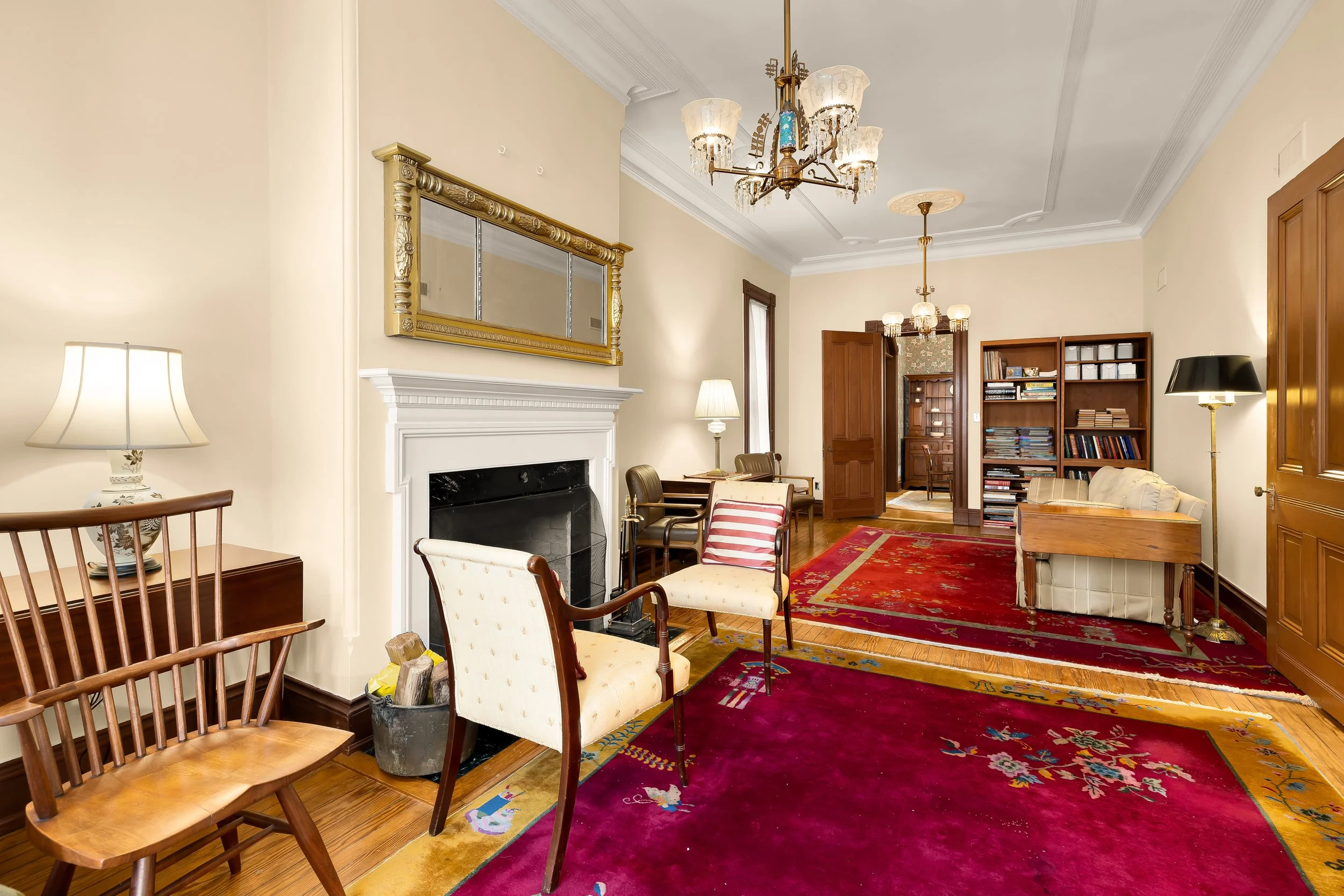 Living room with vintage furniture, colorful area rugs, bookshelf, fireplace, and chandelier