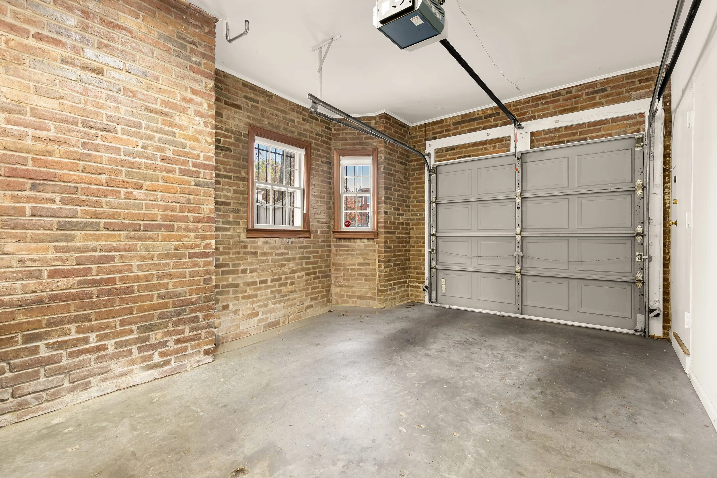 Empty garage with brick walls, two small windows, and a closed gray garage door.