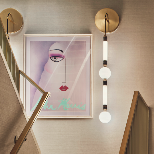 Stairwell with framed artwork, brass handrail and decorative wall light in Studio L London’s St James project