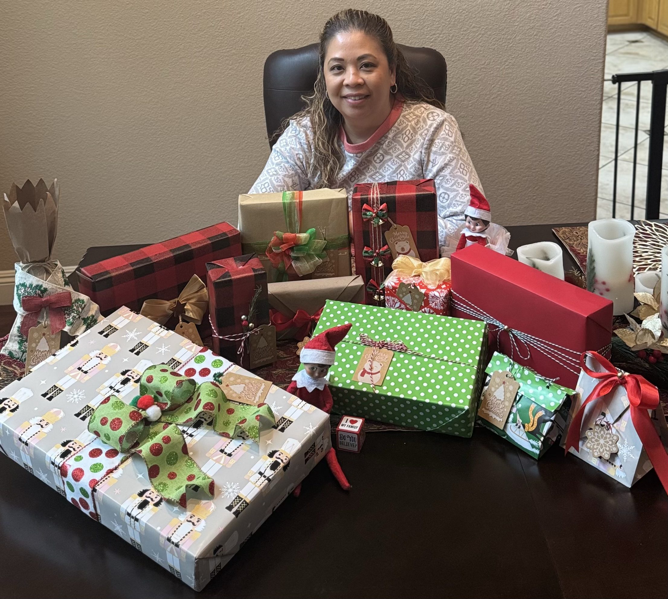A woman sitting at a table with unwrapped Christmas presents and holiday decorations.