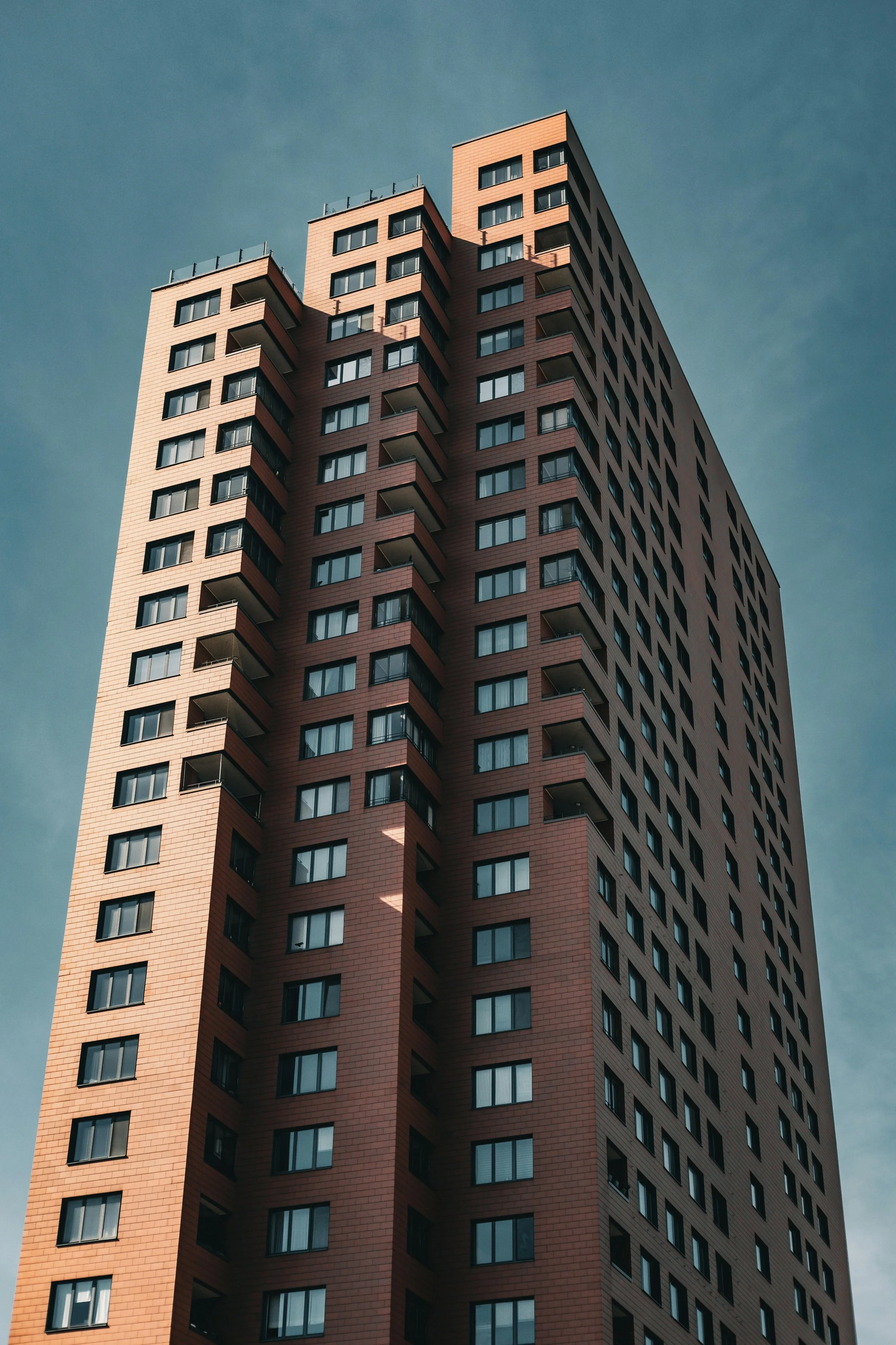 A tall modern apartment building with a distinctive curved design and many windows, set against a clear sky.
