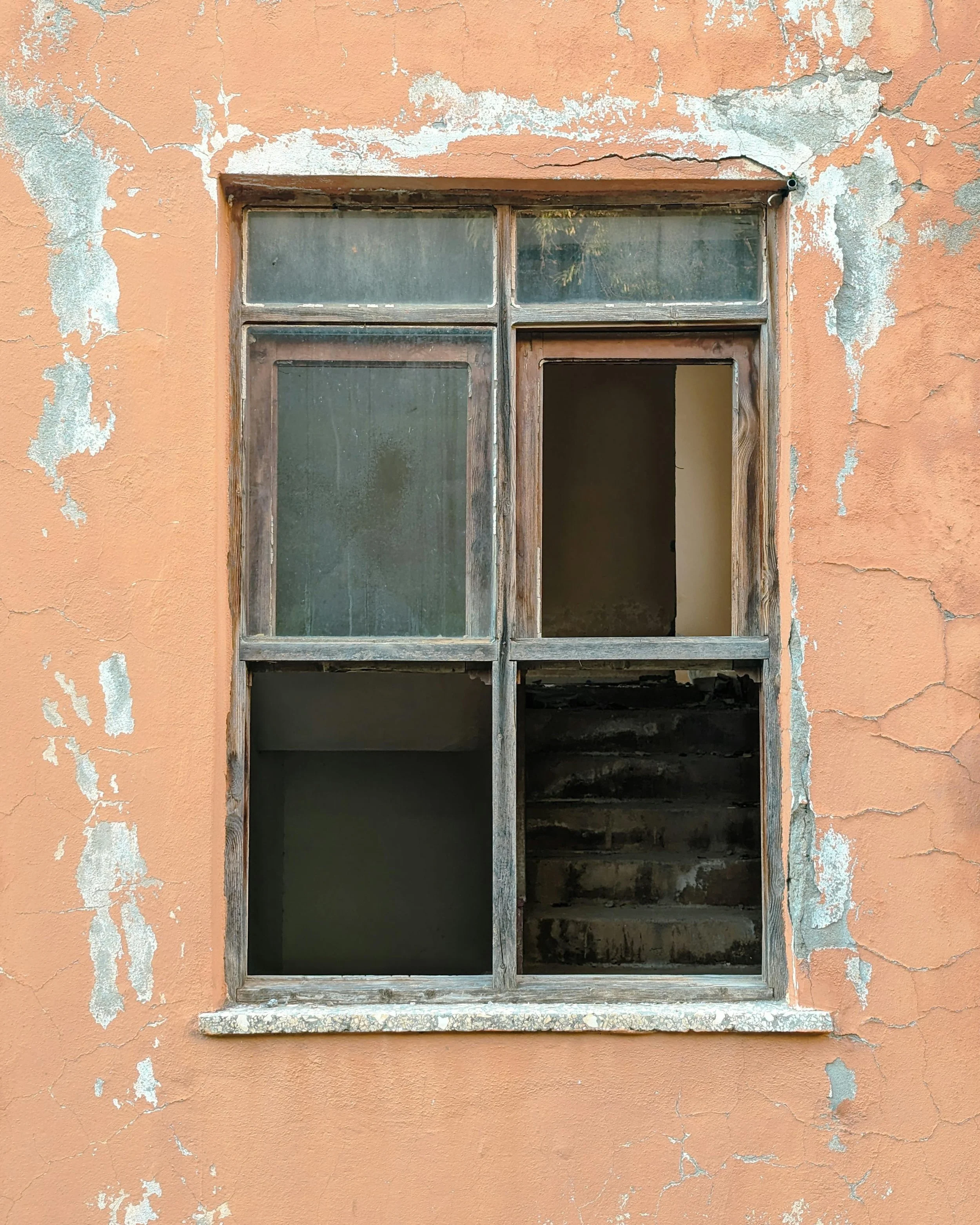 Old, weathered window with peeling paint on a peach-colored wall with cracks.