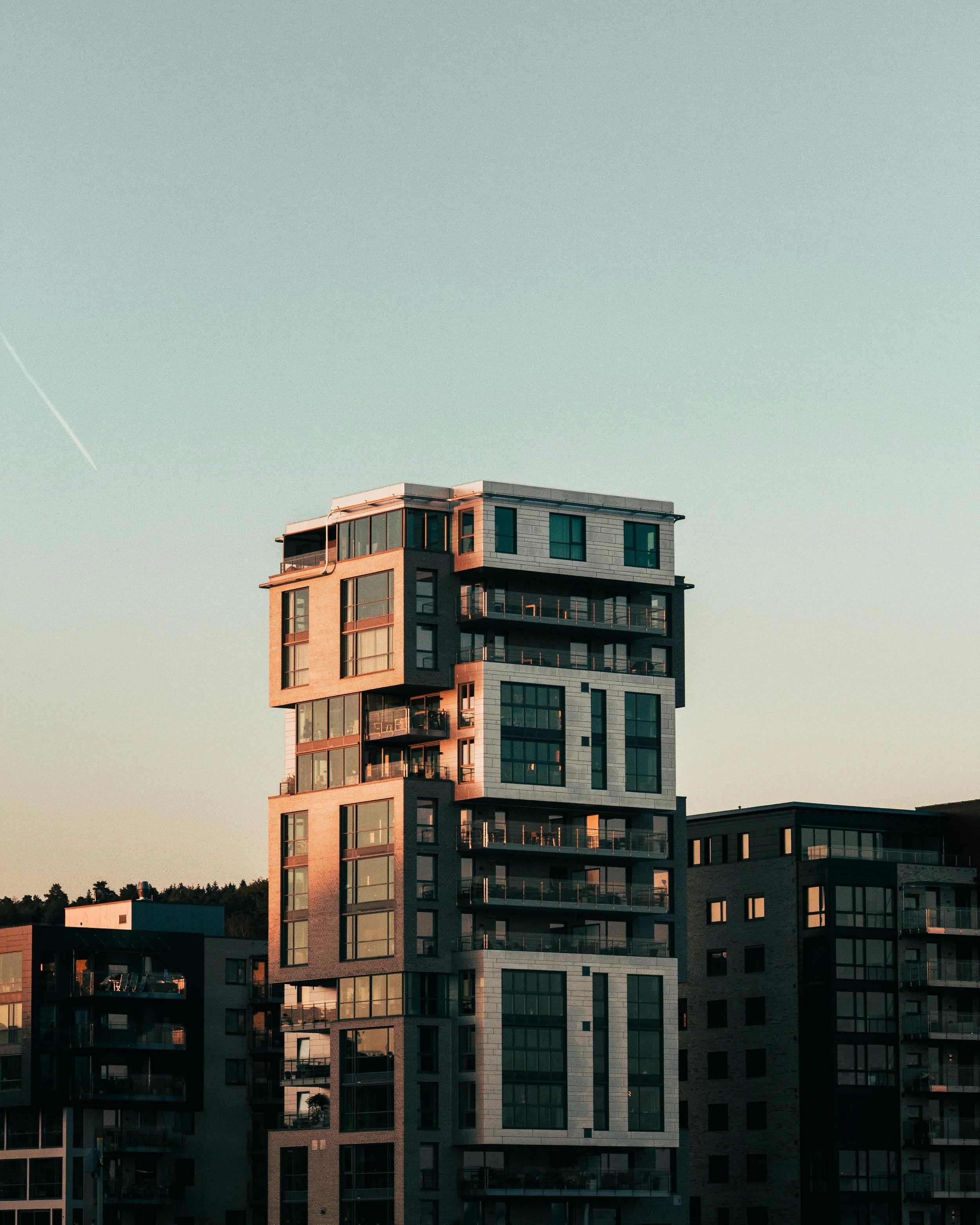Modern high-rise apartment building with multiple balconies, glass windows, and a distinctive architectural design, set against a clear sky during sunset.