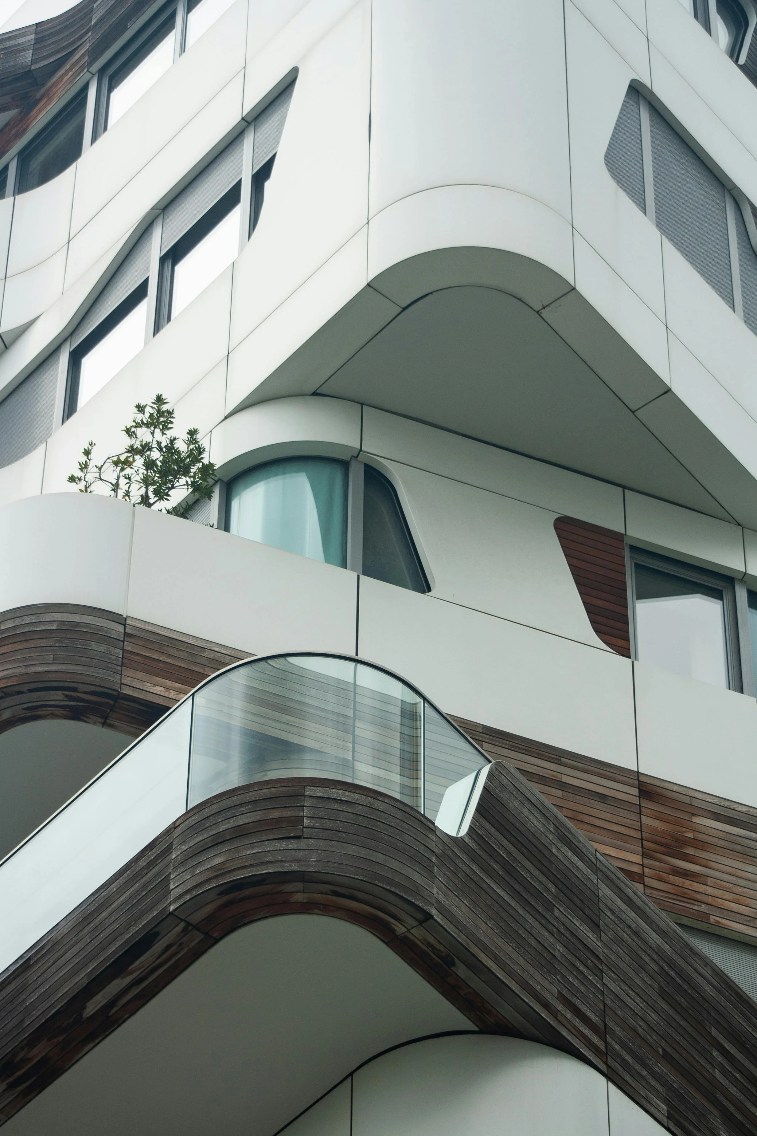 Close-up of a modern building with curved architectural design, white and wooden exterior walls, and glass balcony railing.