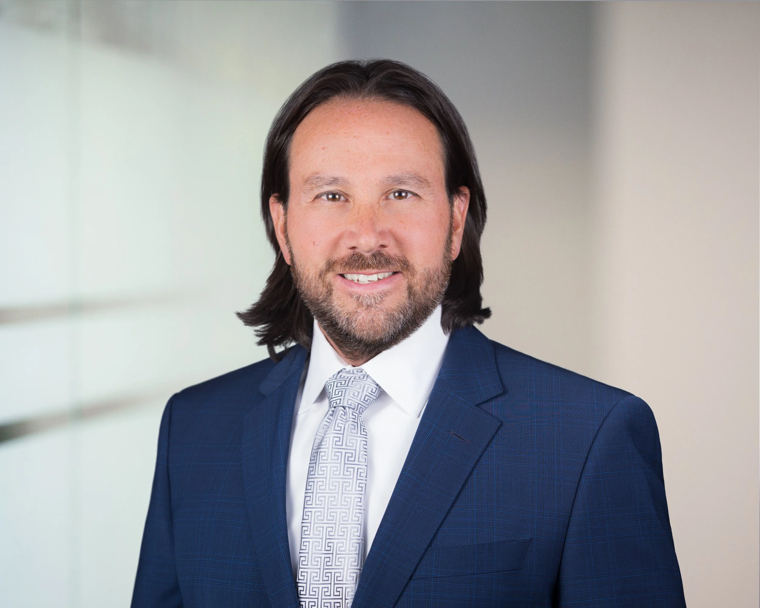 Portrait of a man in a blue suit and patterned tie smiling in a professional setting.