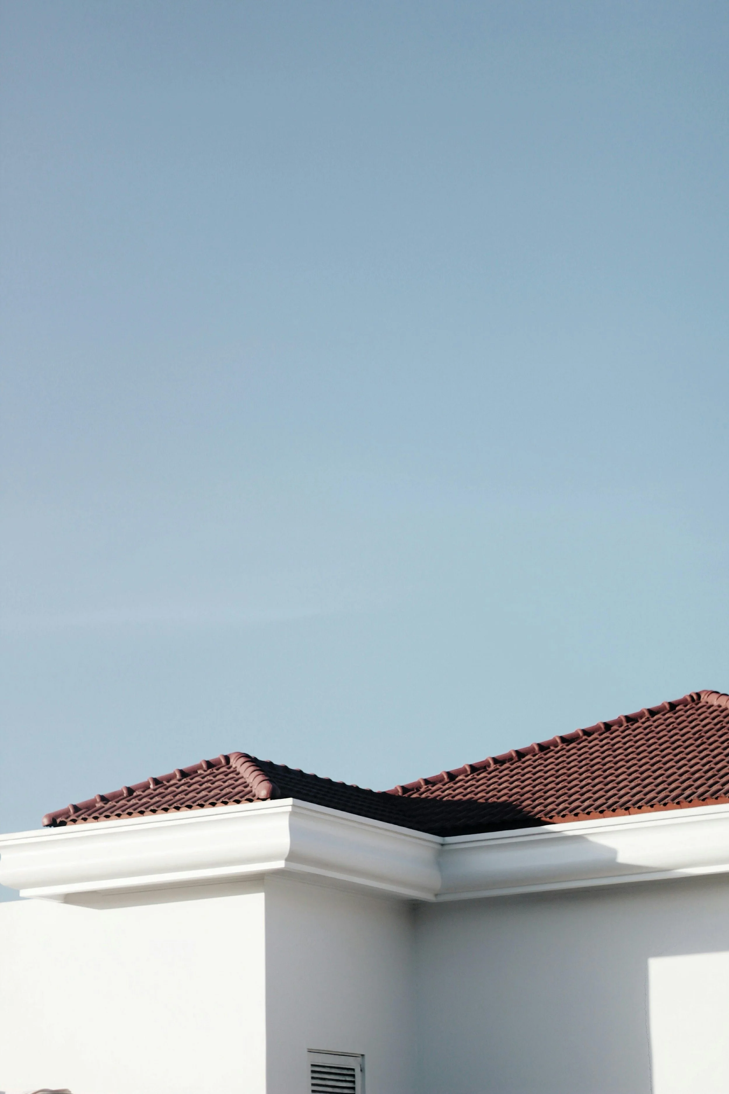 Close-up of a house roof with reddish-brown tiles against a clear blue sky.