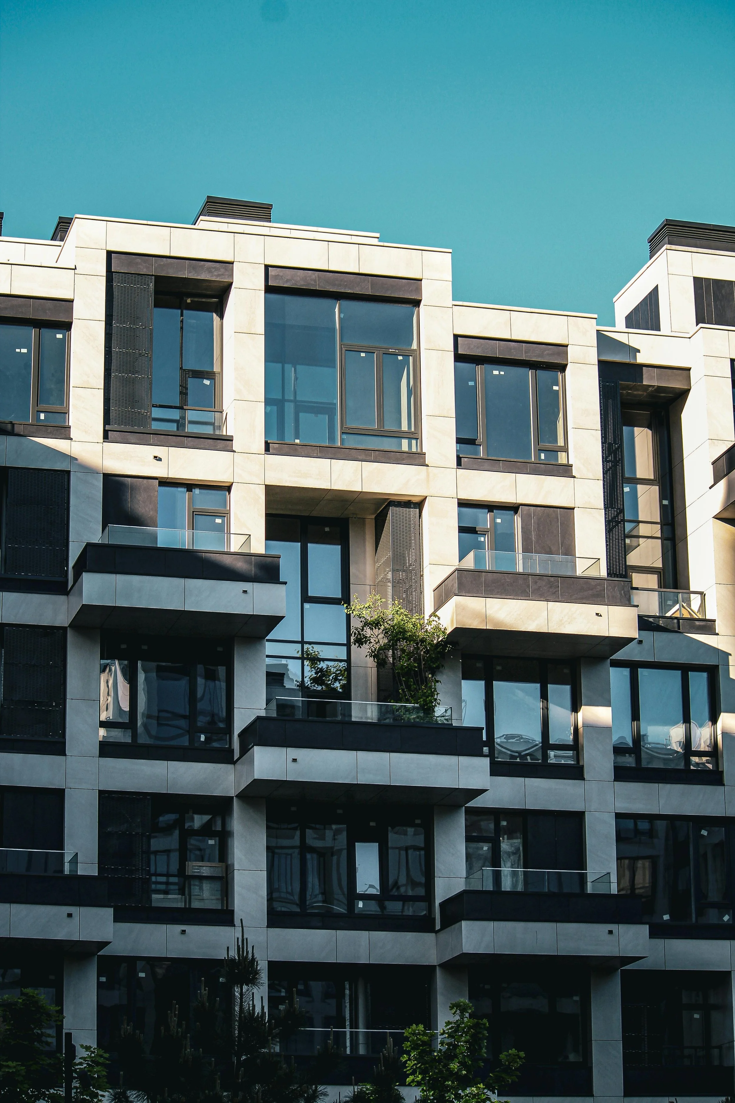 Modern multi-story apartment building with glass windows and balconies under a clear blue sky.