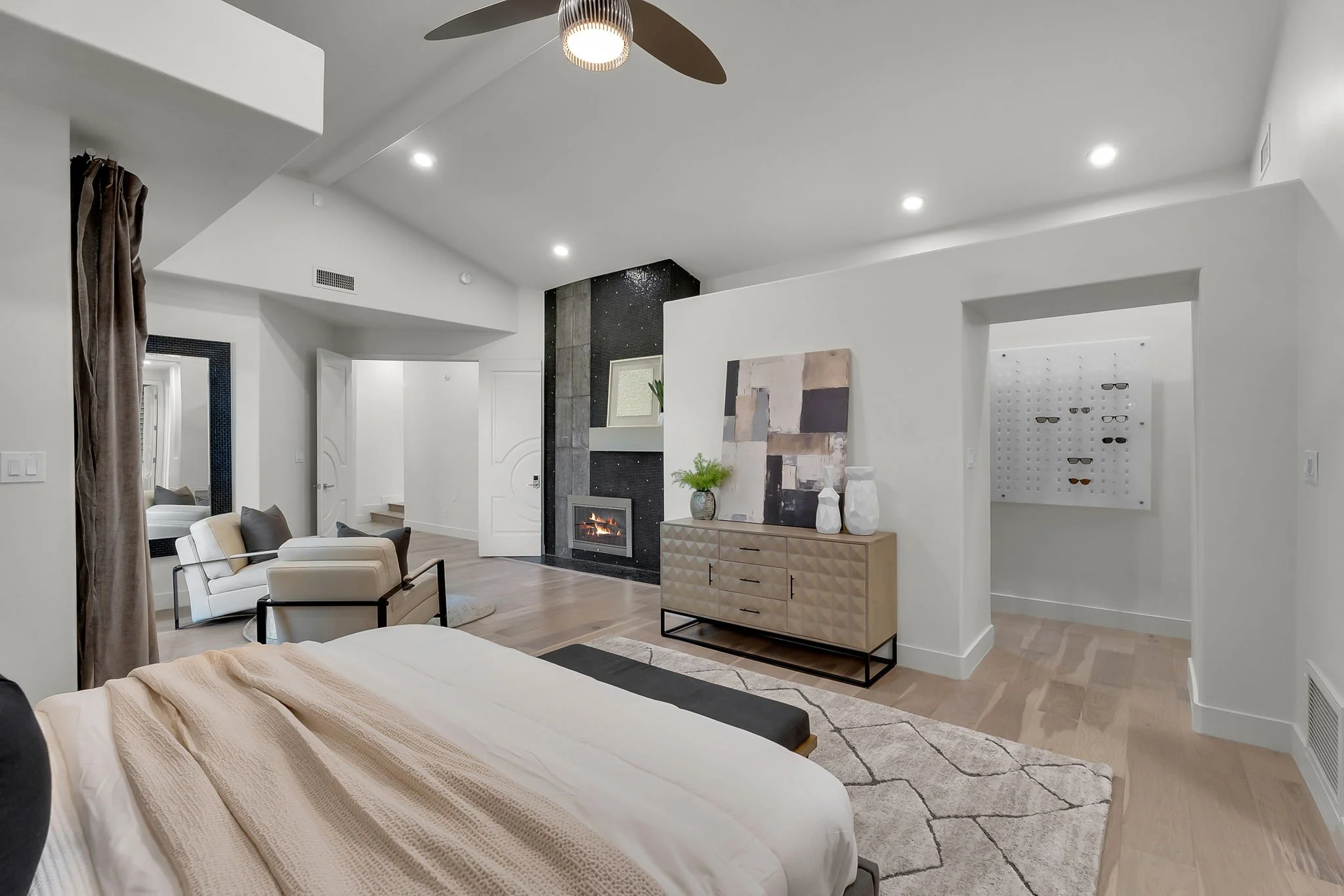 Modern living room with white walls, hardwood floors, a fireplace, a ceiling fan, and contemporary furniture.