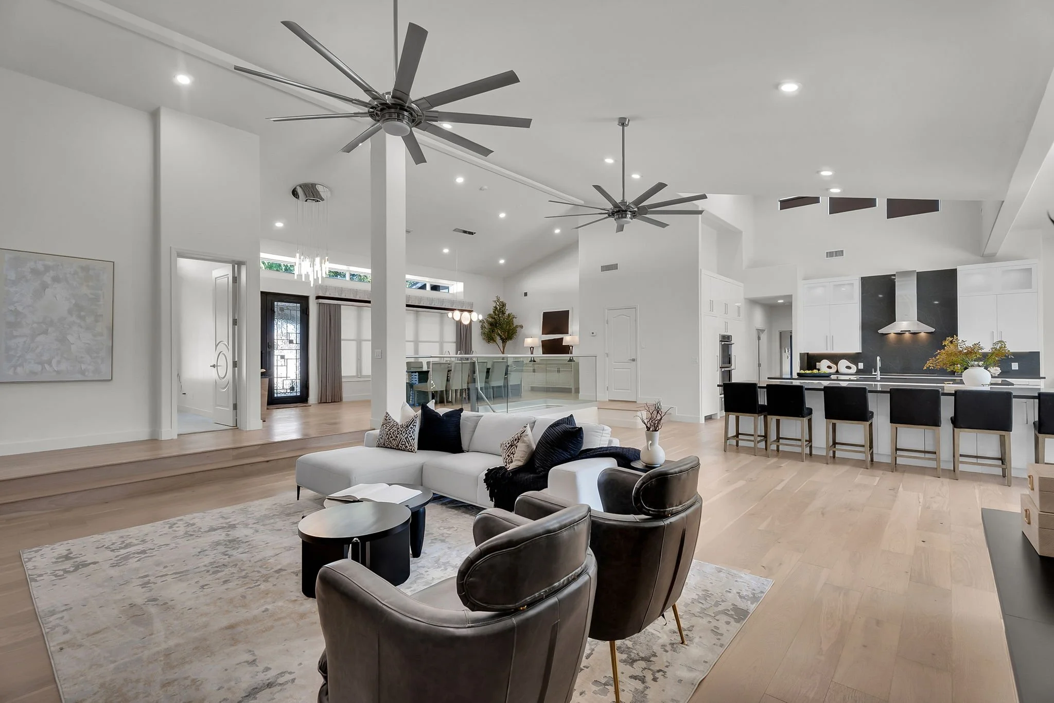 Open-concept living room and kitchen with high ceilings, ceiling fans, modern furniture, and abundant natural light.