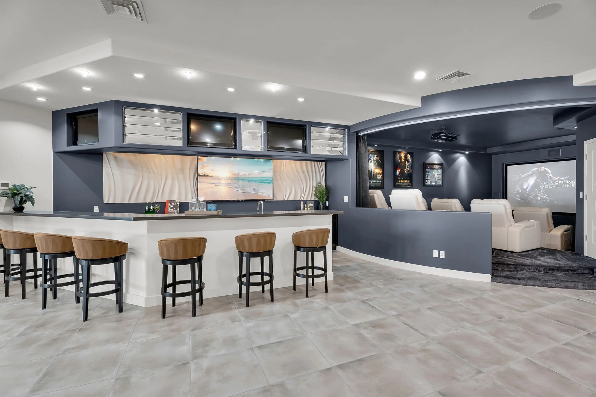 Modern home theater room with a large-screen TV, white leather recliners, and a bar area with barstools.