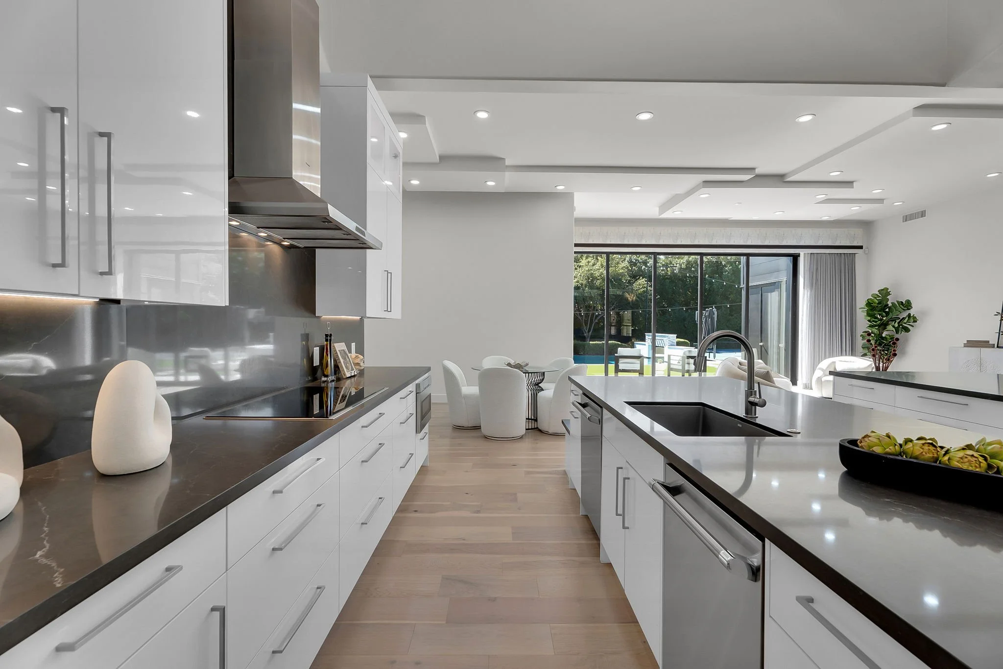 Modern kitchen with white cabinetry, black countertops, a kitchen island with a sink, and a view of a patio with outdoor furniture and a swimming pool.