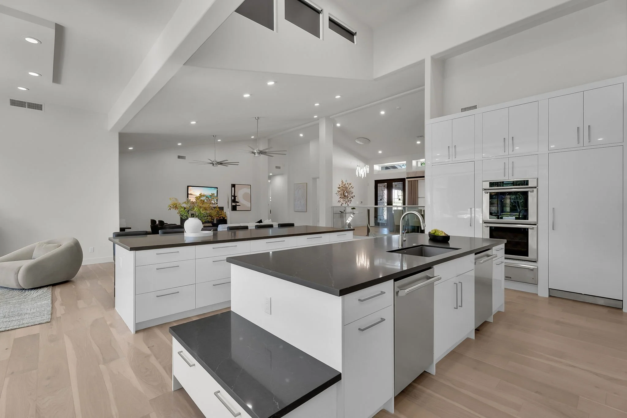 Modern open-concept kitchen with white cabinets and black countertops, hardwood floors, island with sink, and adjacent living area with a beige chair.