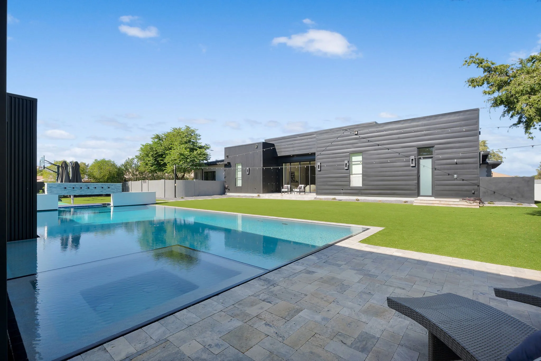 Modern backyard with a rectangular swimming pool, green lawn, and black house with large windows and a sliding door.