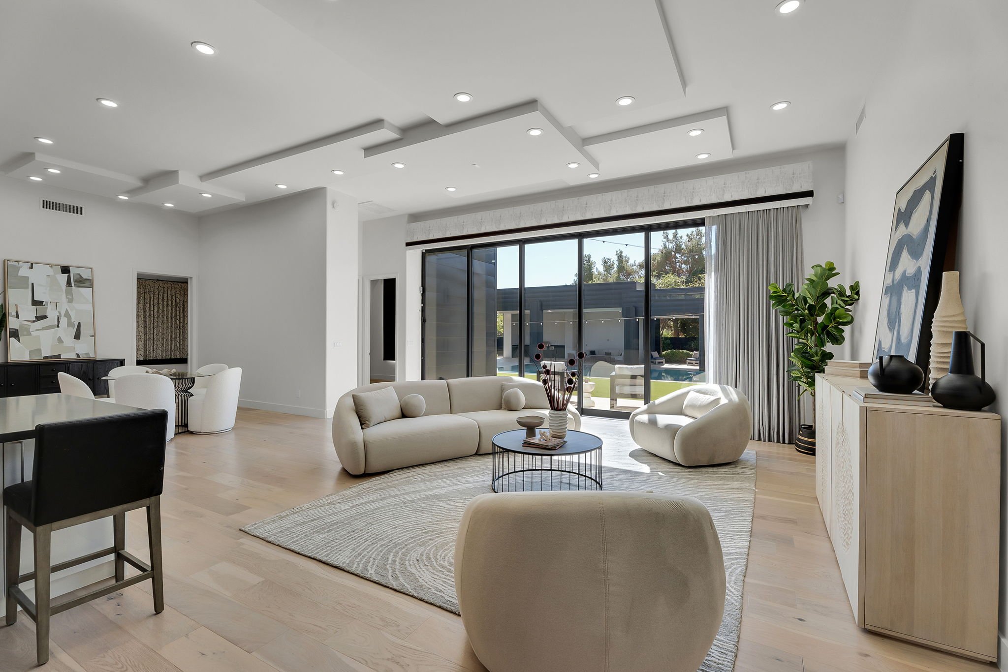 Modern living room with white walls, cream furniture, a large sliding glass door, and a light wood floor.