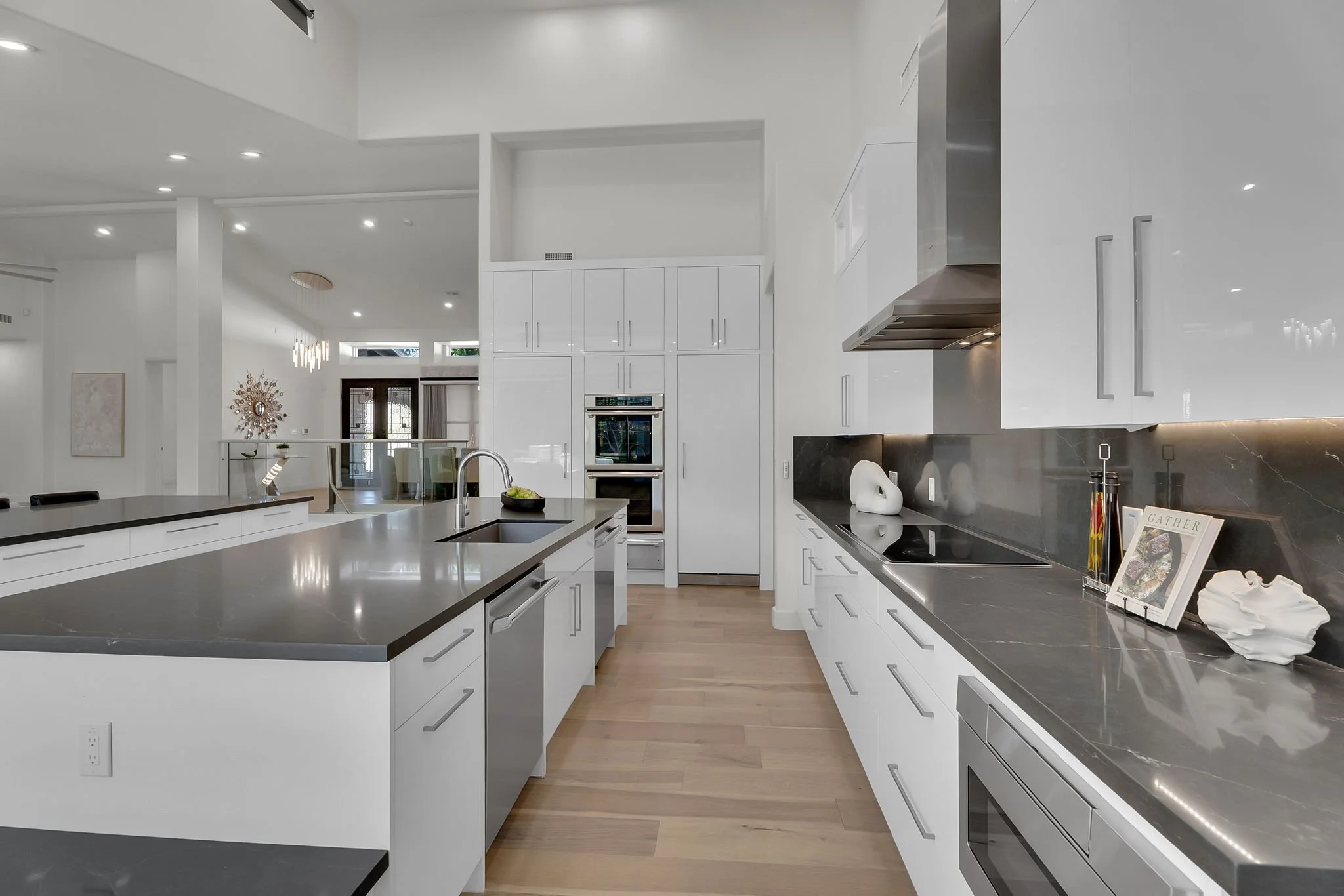 Modern kitchen with white cabinets, gray countertops, and hardwood floors, featuring a sink, stove, and decorative items.