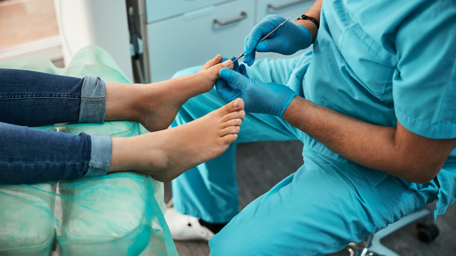 A healthcare worker in scrubs and gloves holding a patient's hand while preparing to draw blood or insert an IV line in a medical clinic or hospital setting.