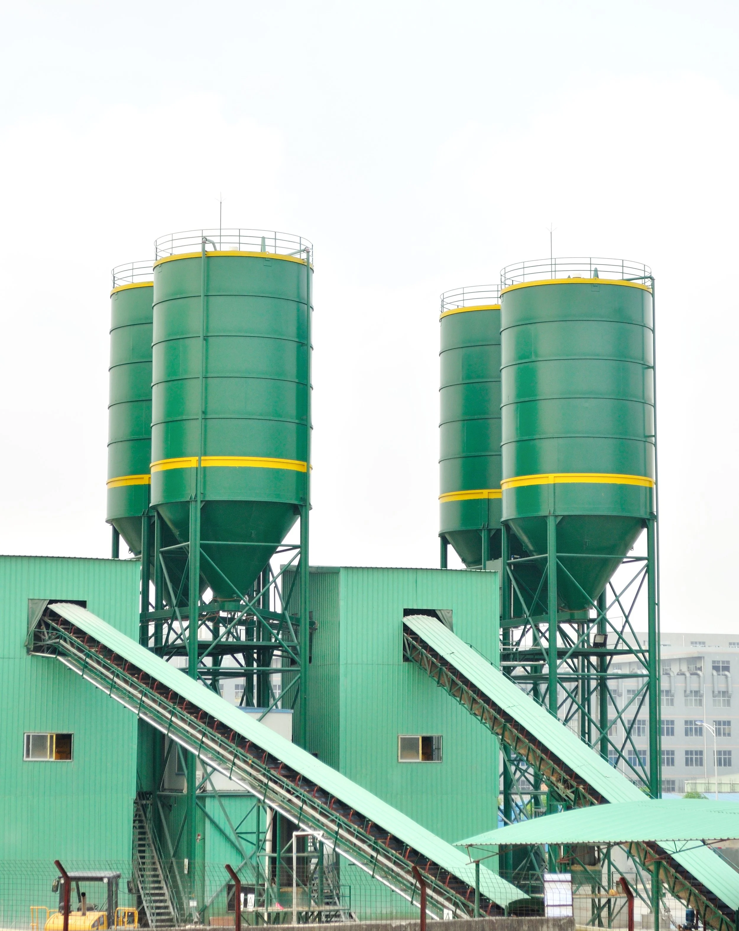 Industrial facility with four green storage tanks and conveyor belts.