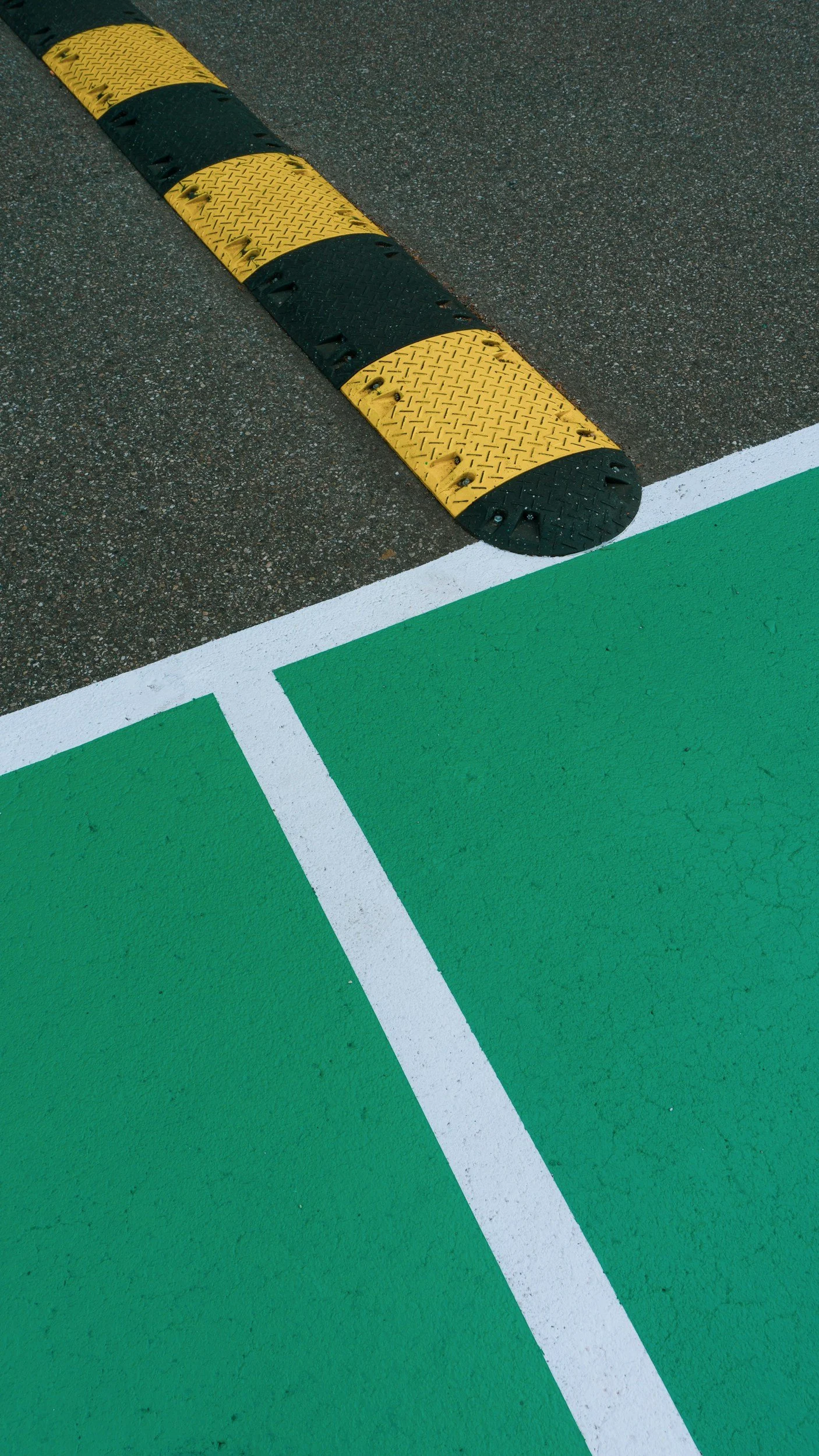 Close-up of a black and yellow speed bump next to green and white painted road markings on asphalt.